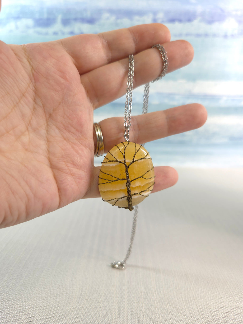 Hand holding a necklace with a yellow stone pendant against a blurred natural background