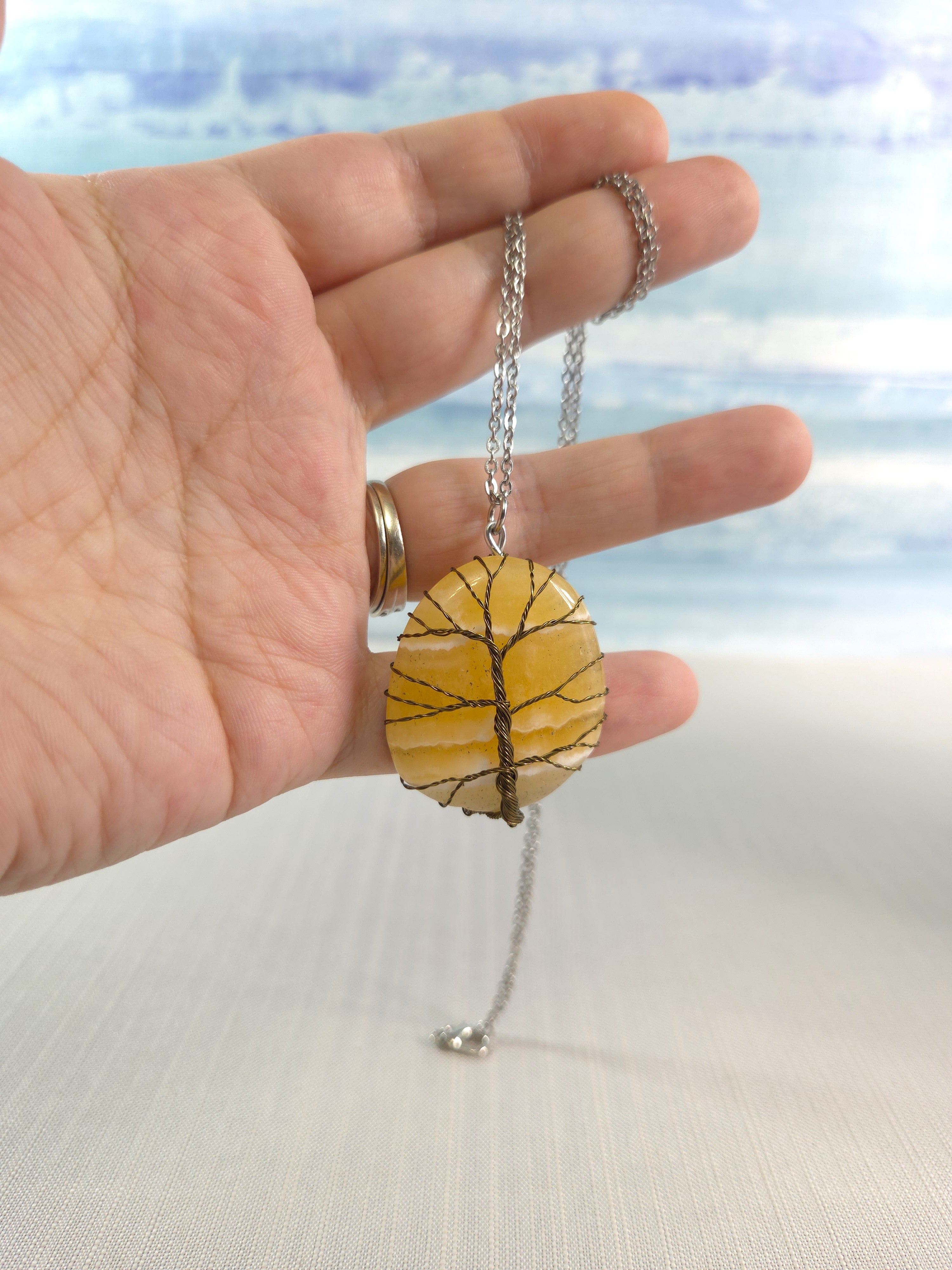 Hand holding a necklace with a yellow stone pendant against a blurred natural background