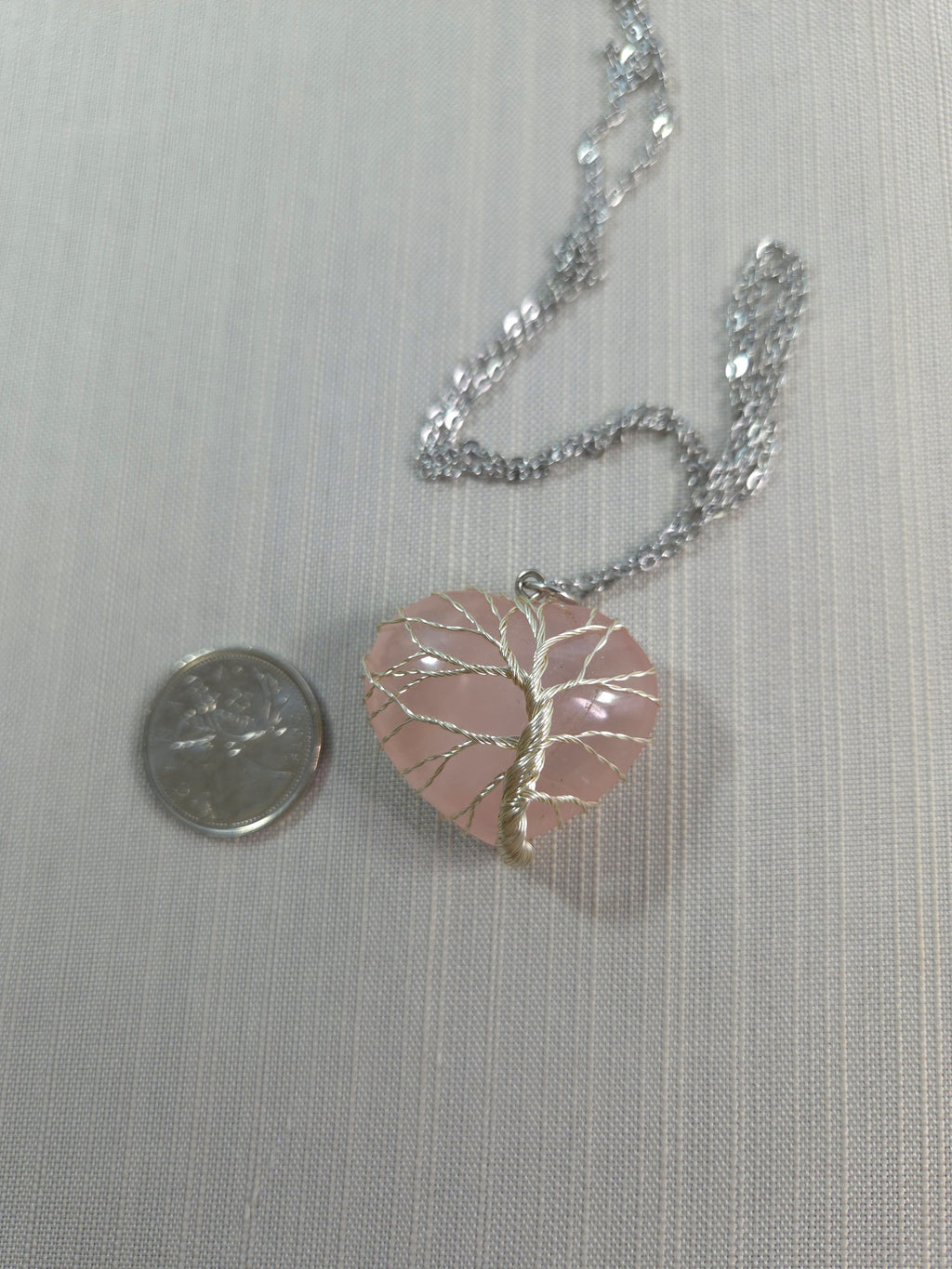 Necklace with a pink heart-shaped pendant next to a quarter on a light gray background