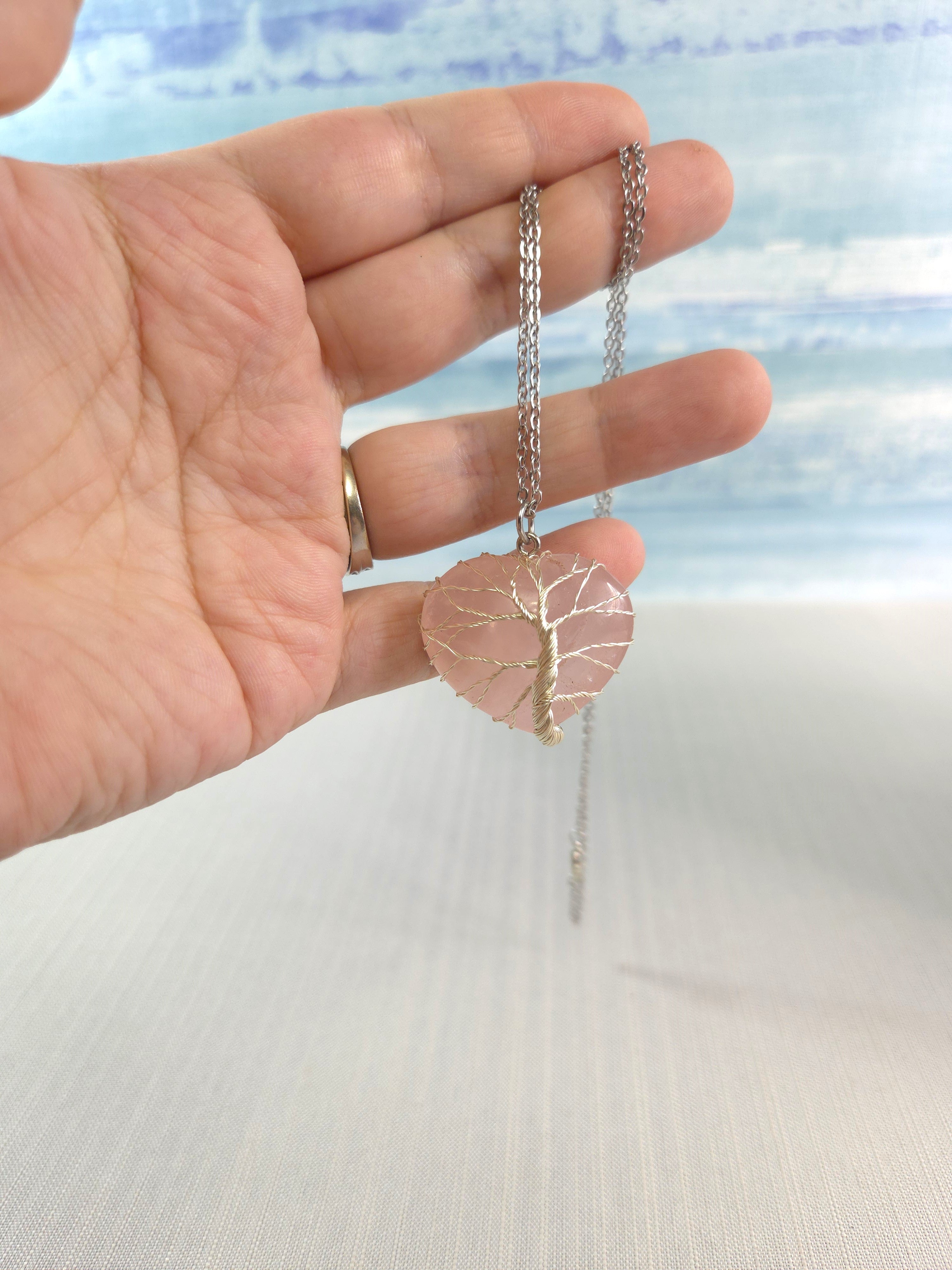 Hand holding a silver necklace with a pink pendant against a blurred natural background
