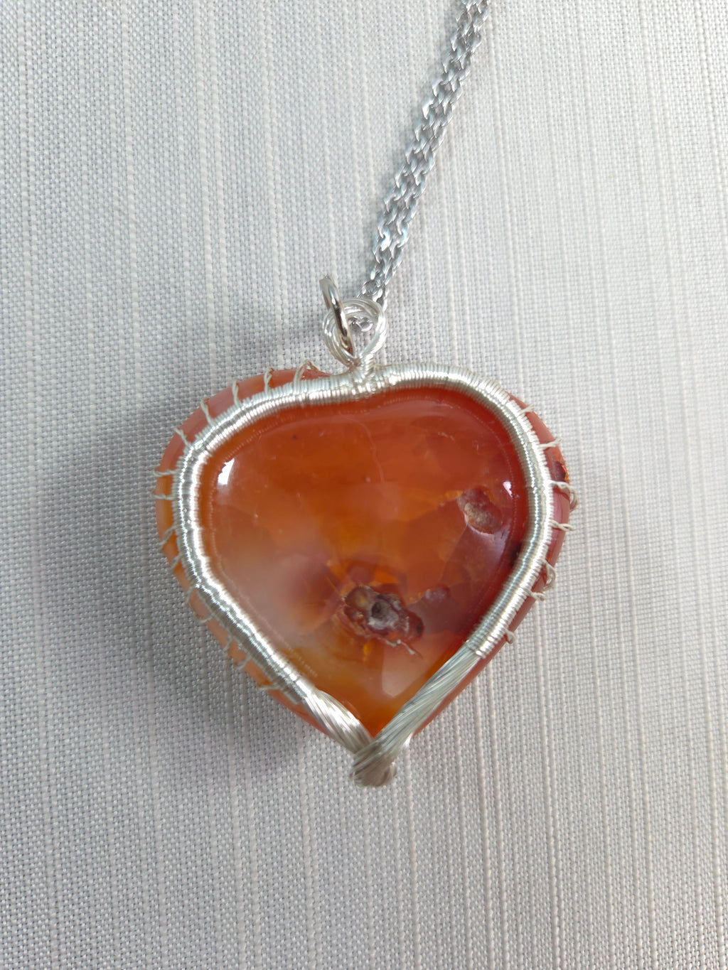 Necklace with a pendant featuring a large orange stone and silver wire wrapping on a light gray background.