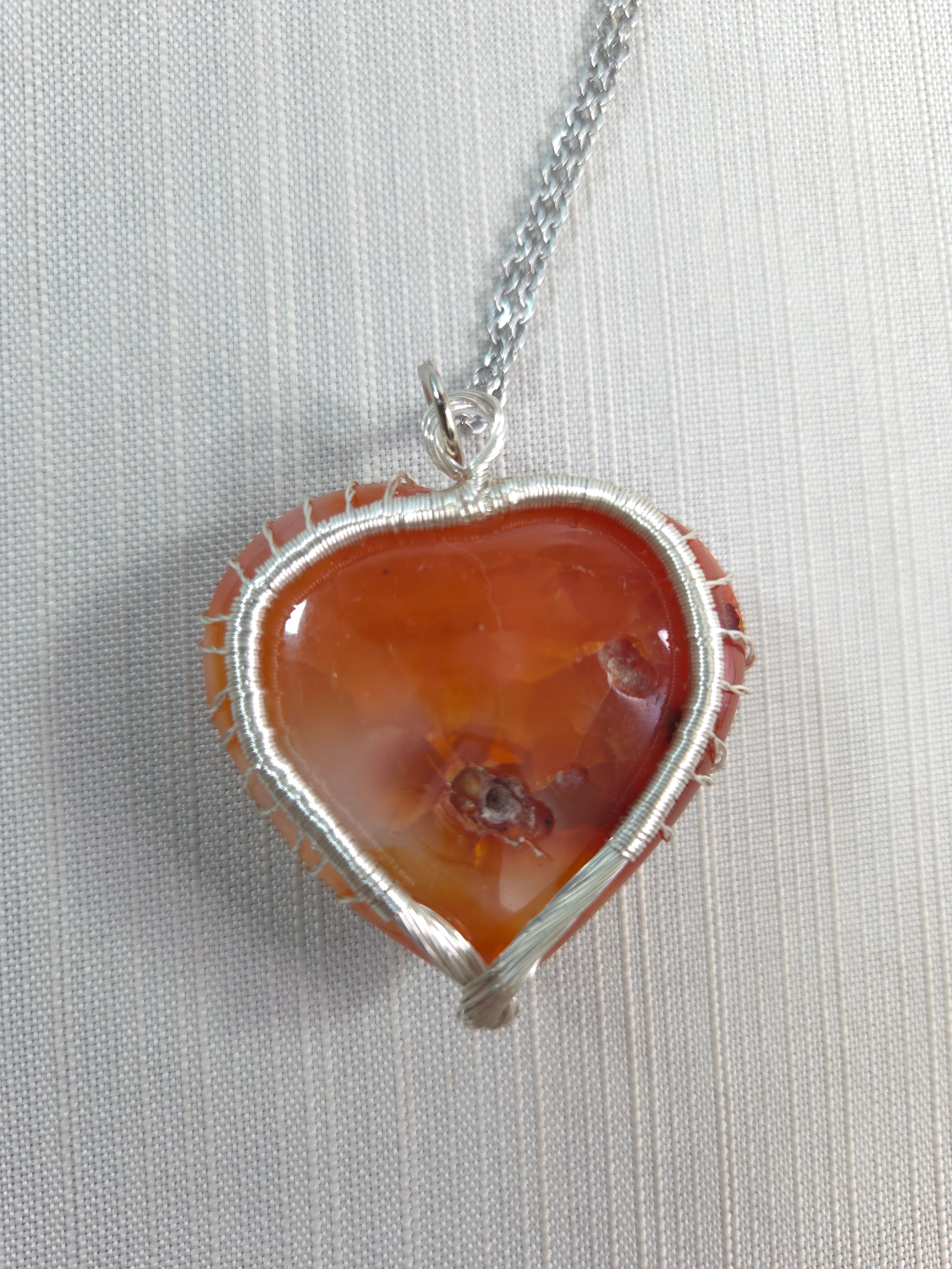 Necklace with a pendant featuring a large orange stone and silver wire wrapping on a light gray background.