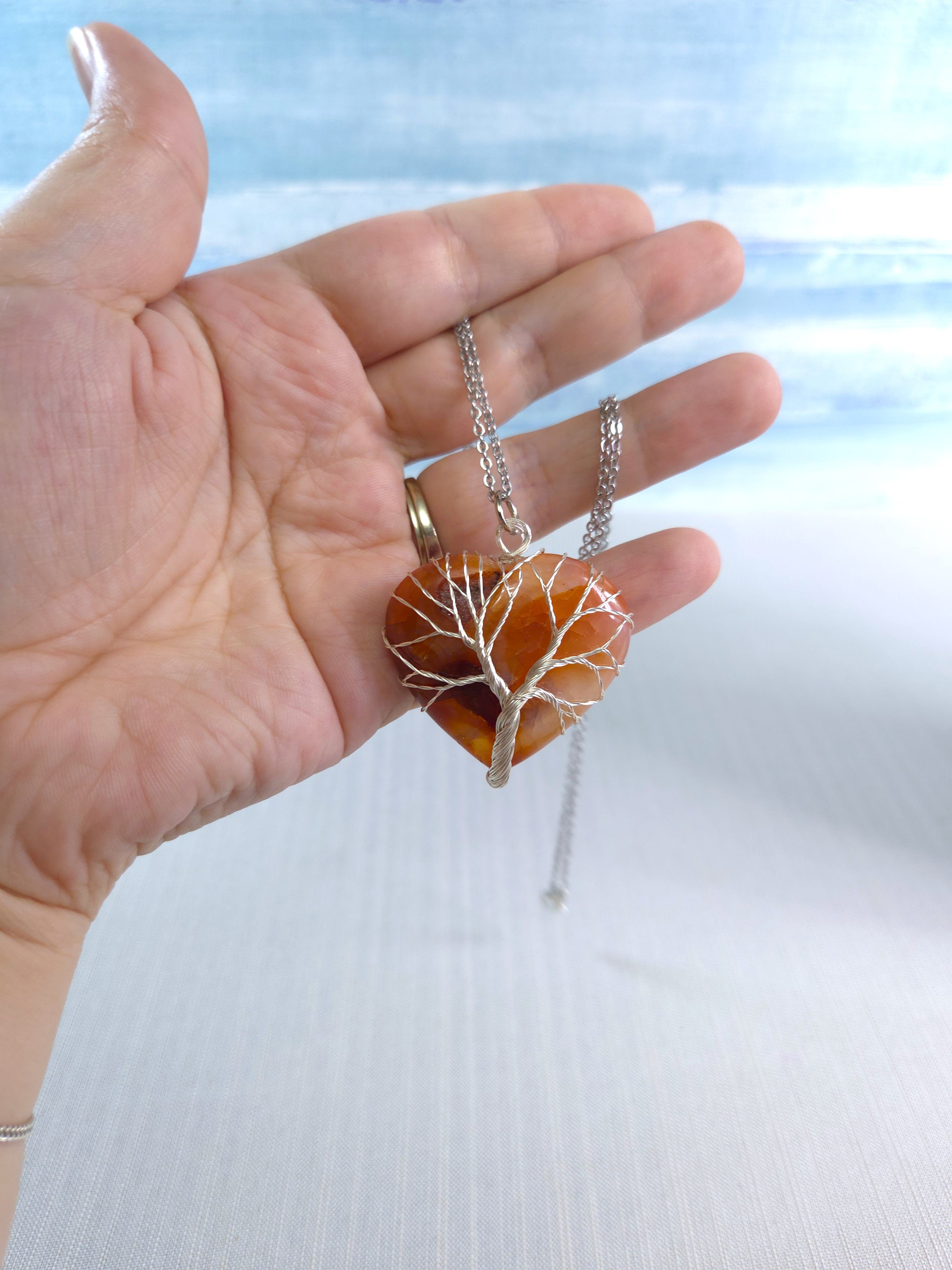 Hand holding a necklace with a tree pendant against a blurred natural background