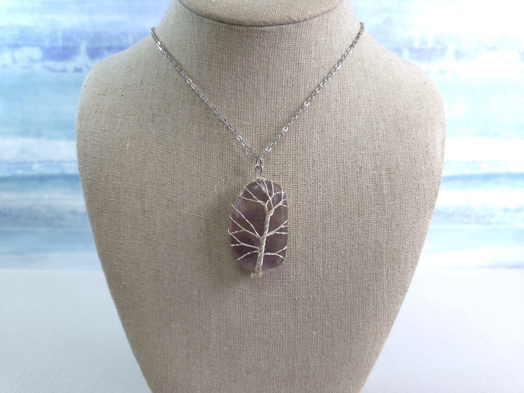 Necklace with a tree-shaped pendant on a mannequin bust against a blurred beach background