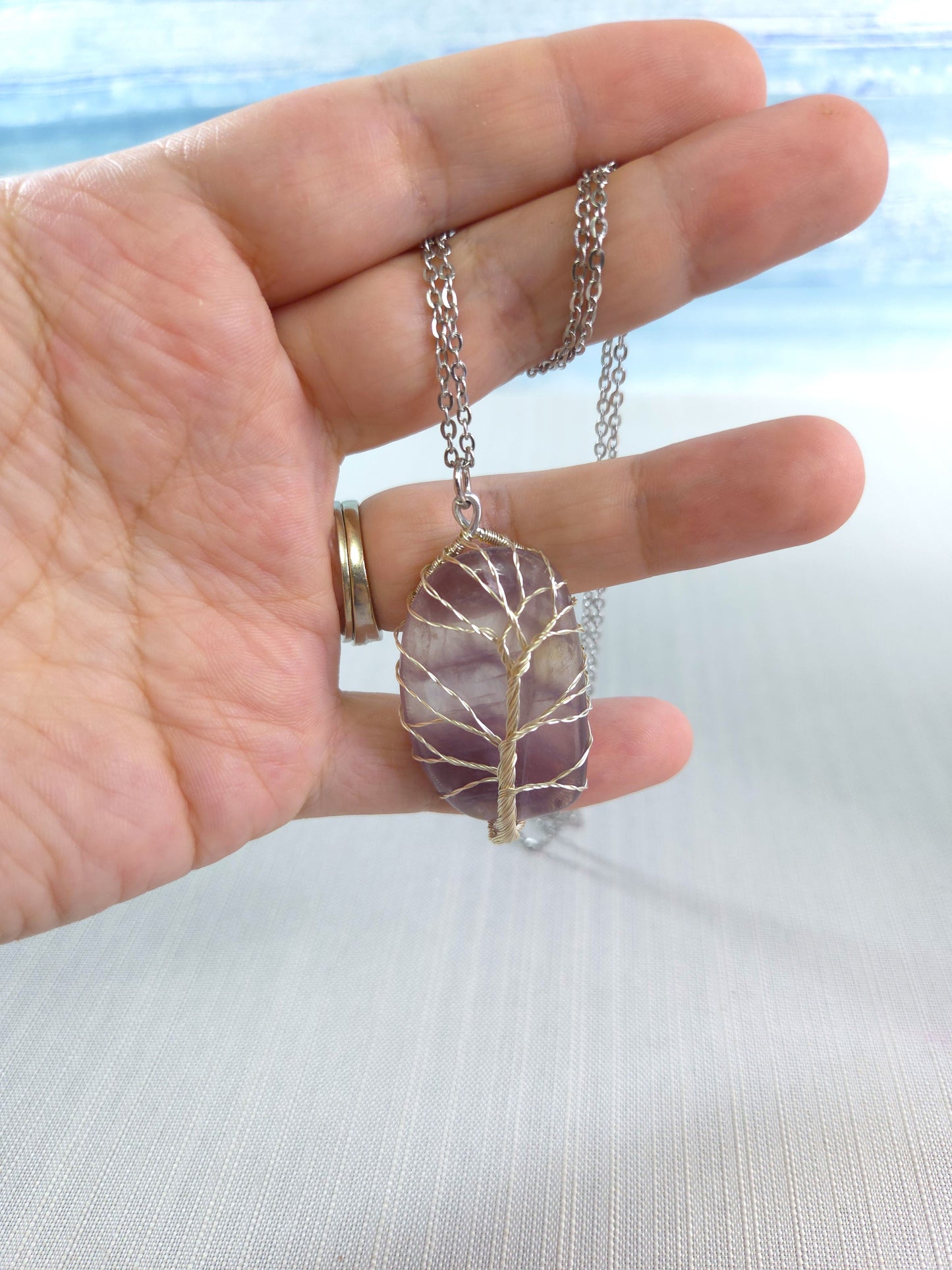 Hand holding a necklace with a tree-of-life pendant against a light background