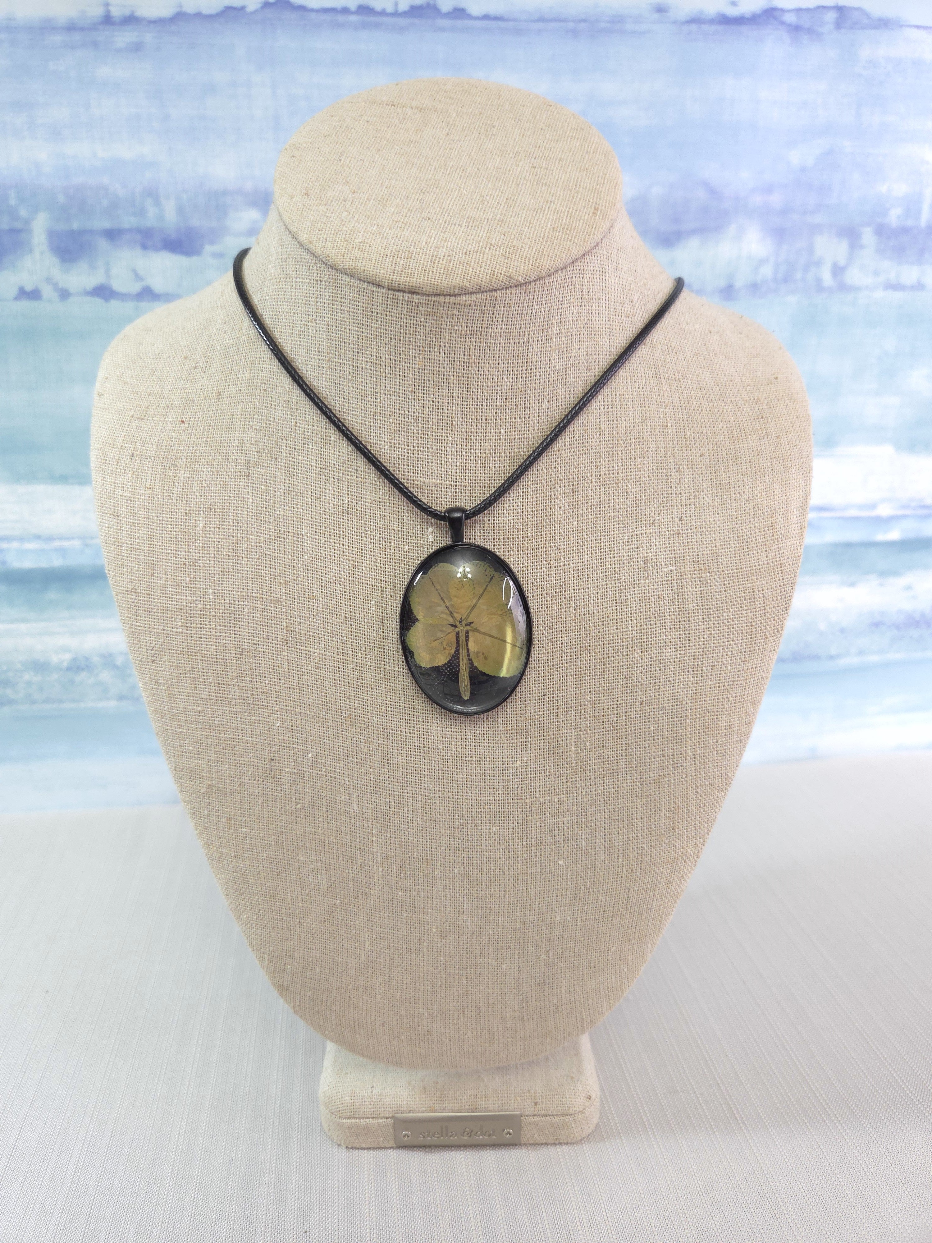 Necklace with a clover pendant on a beige bust against a light blue watercolor background