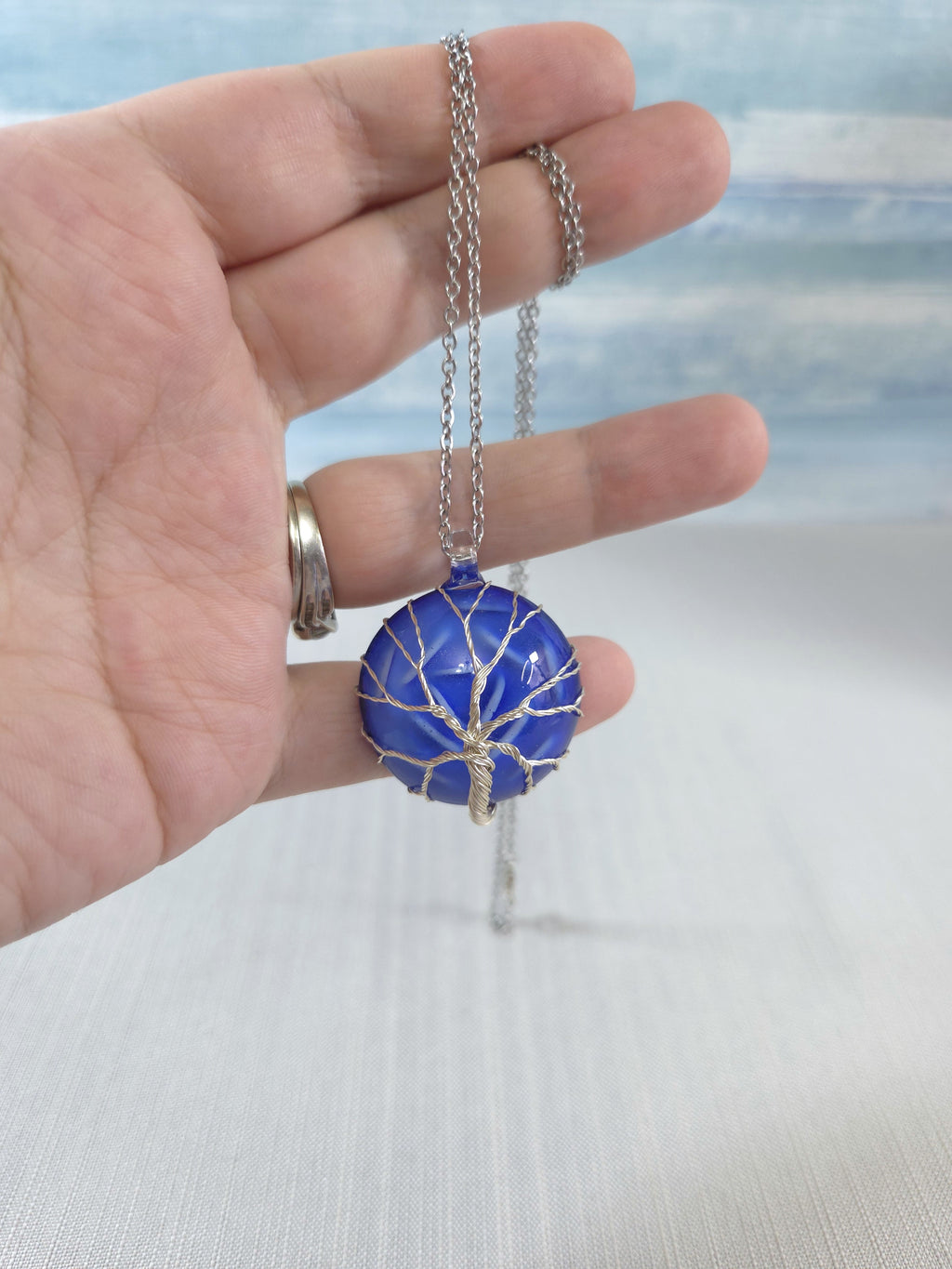 Hand holding a necklace with a blue pendant against a blurred background