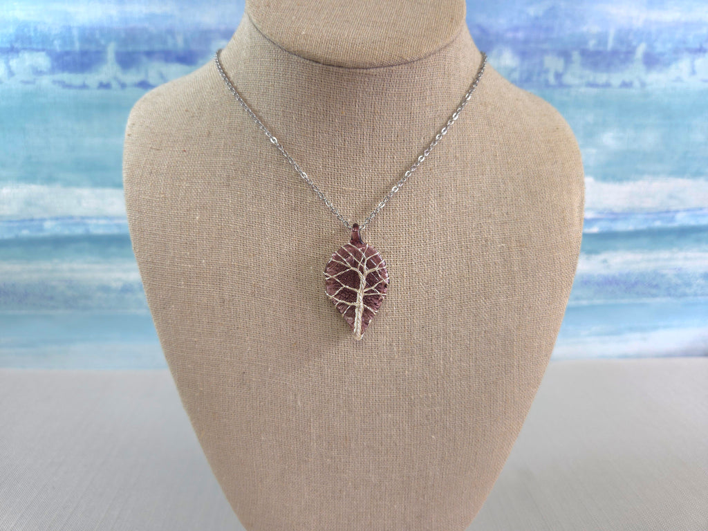 Leaf-shaped pendant necklace on a mannequin bust with a blurred beach background