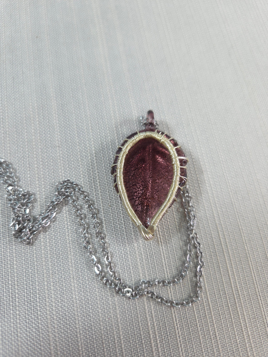 Teardrop-shaped pendant with a chain on a light gray background