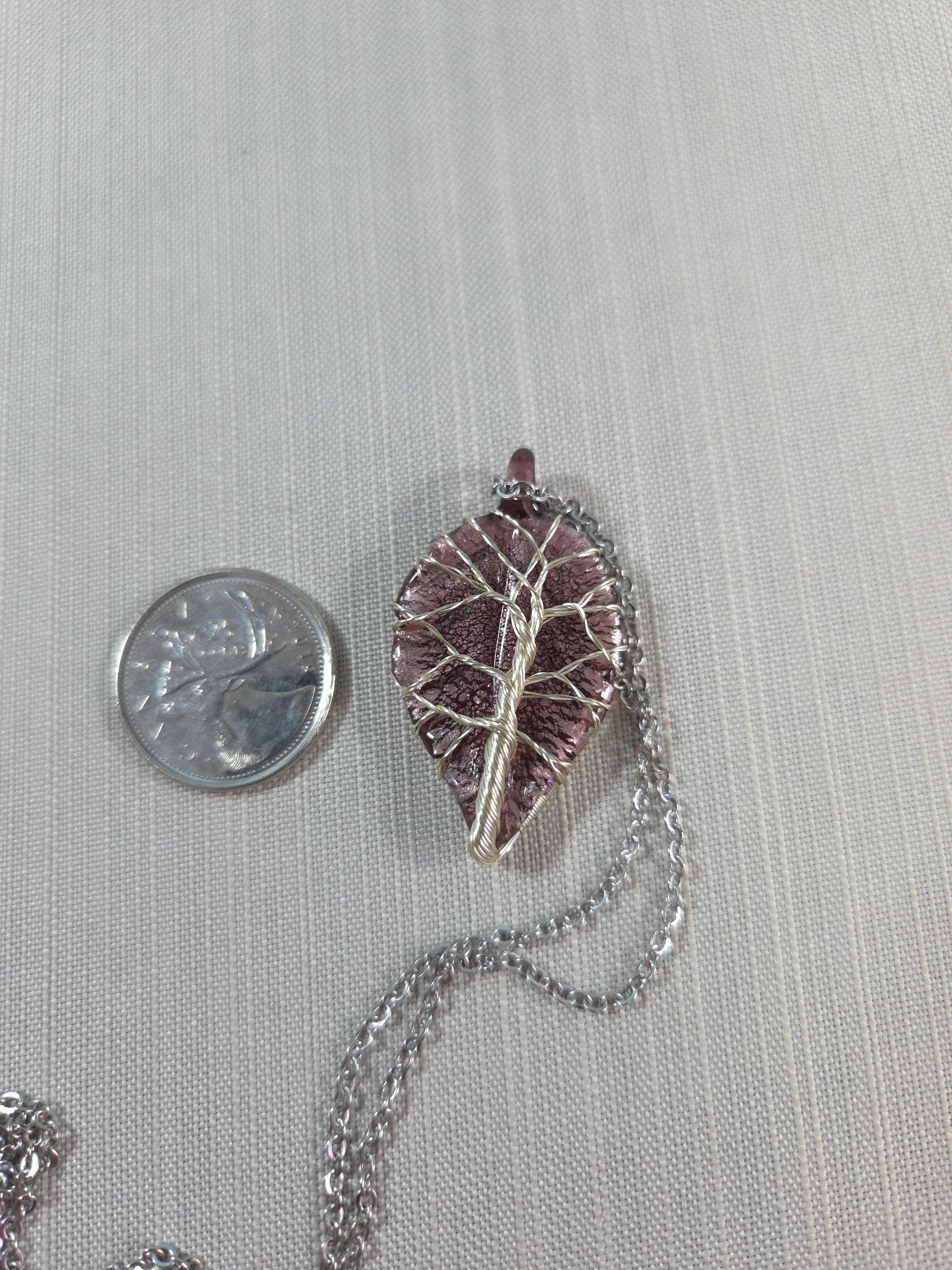 Silver leaf-shaped pendant on a chain with a quarter for scale on a gray background