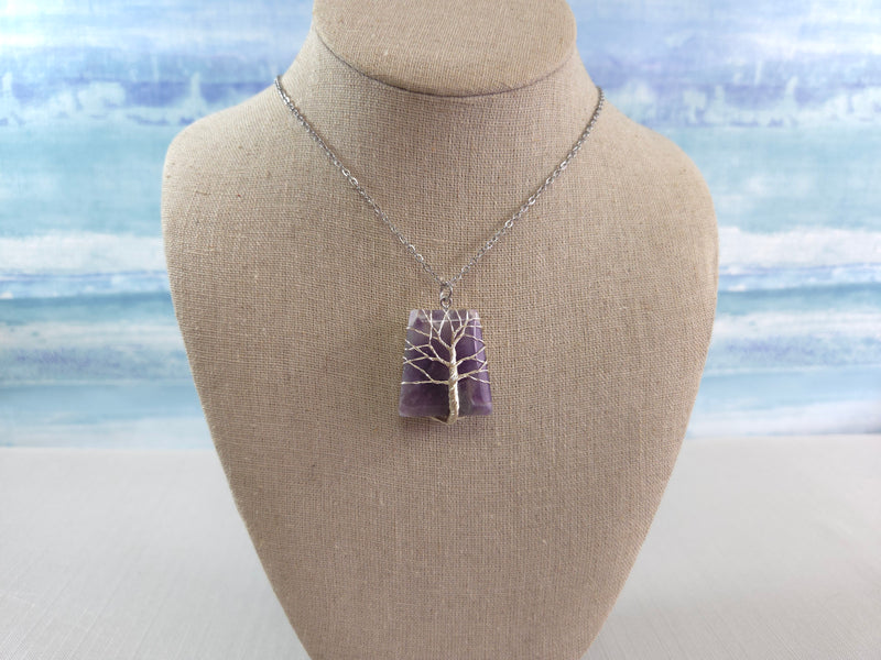 Necklace with a purple tree of life pendant on a mannequin bust against a beach background