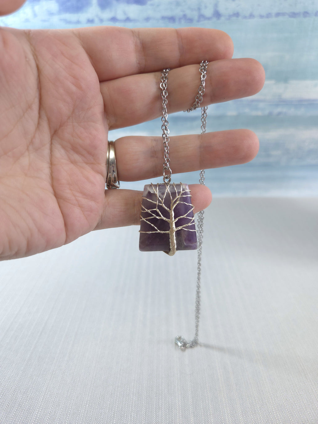 Hand holding a necklace with a tree-of-life pendant against a blurred background