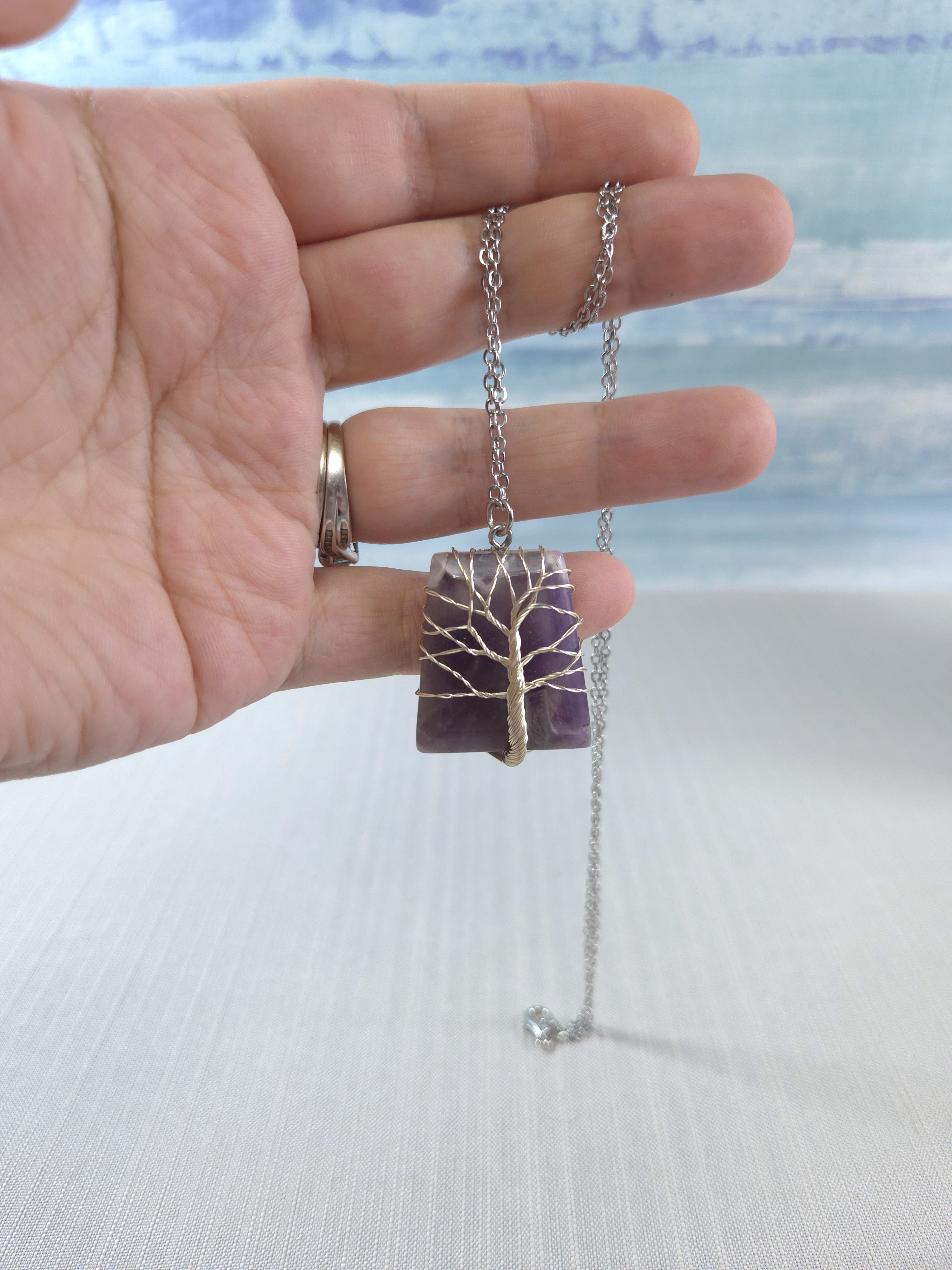 Hand holding a necklace with a tree-of-life pendant against a blurred background