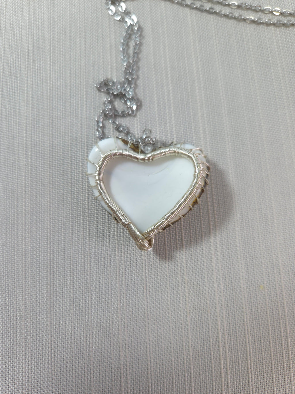 Heart-shaped pendant on a chain against a textured gray background