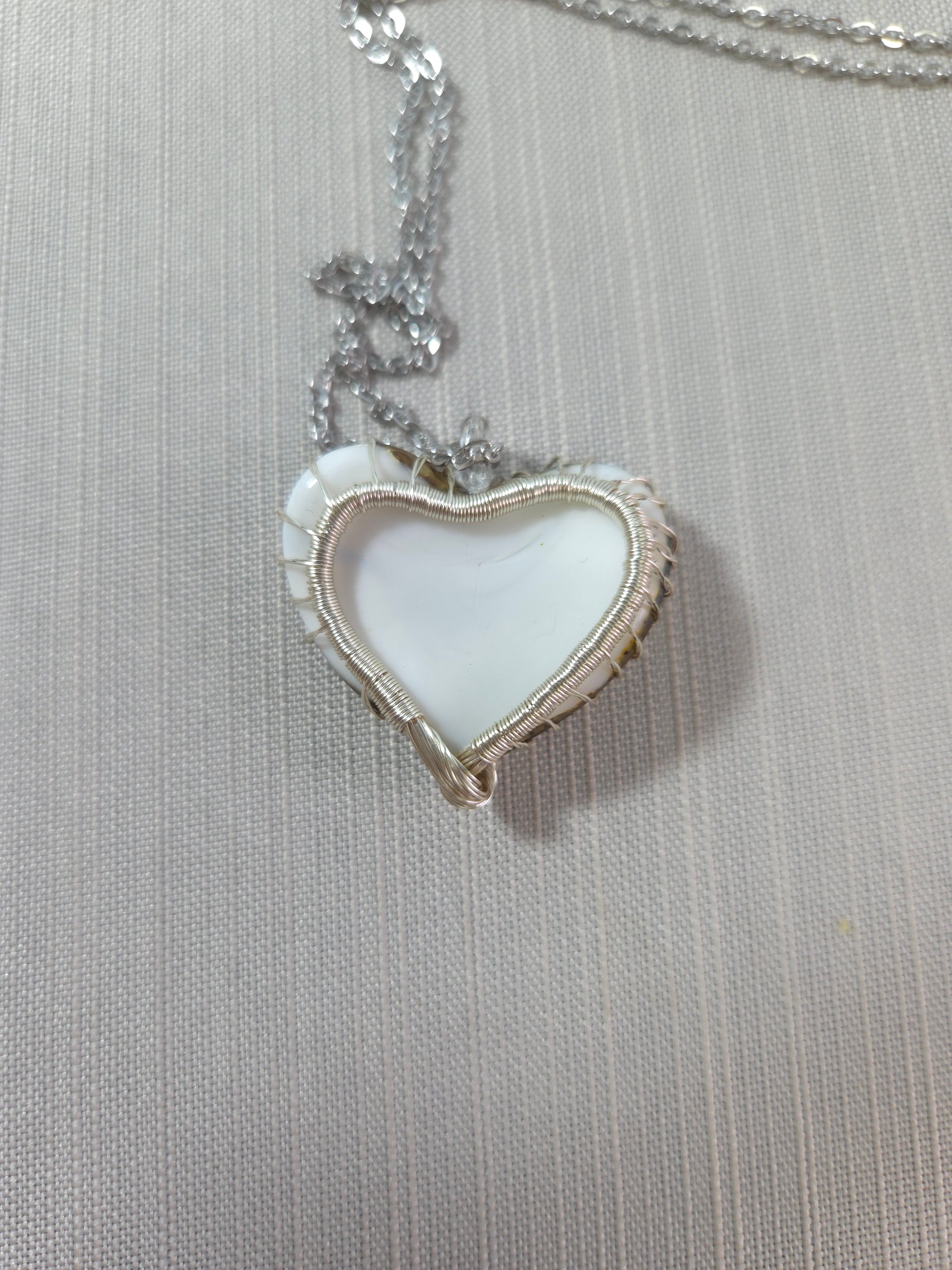 Heart-shaped pendant on a chain against a textured gray background