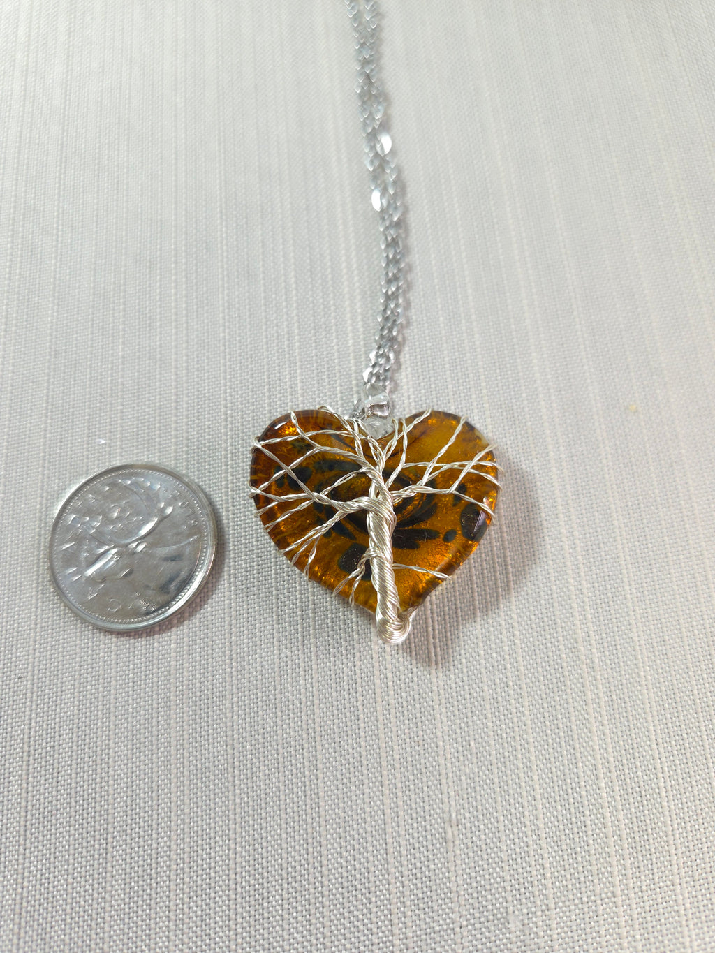 Tiger eye stone pendant on a silver chain with a quarter for scale on a light gray background