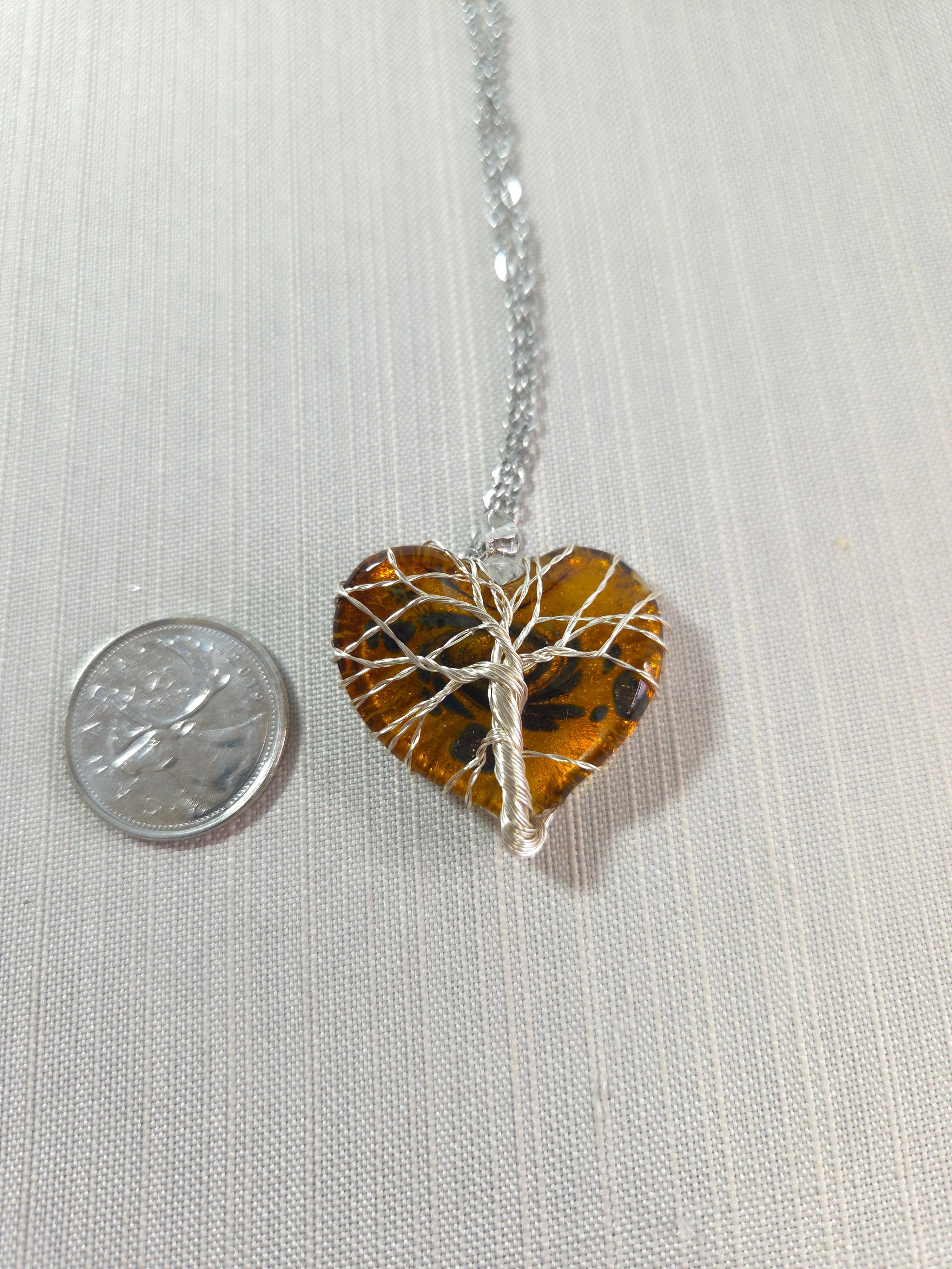 Tiger eye stone pendant on a silver chain with a quarter for scale on a light gray background