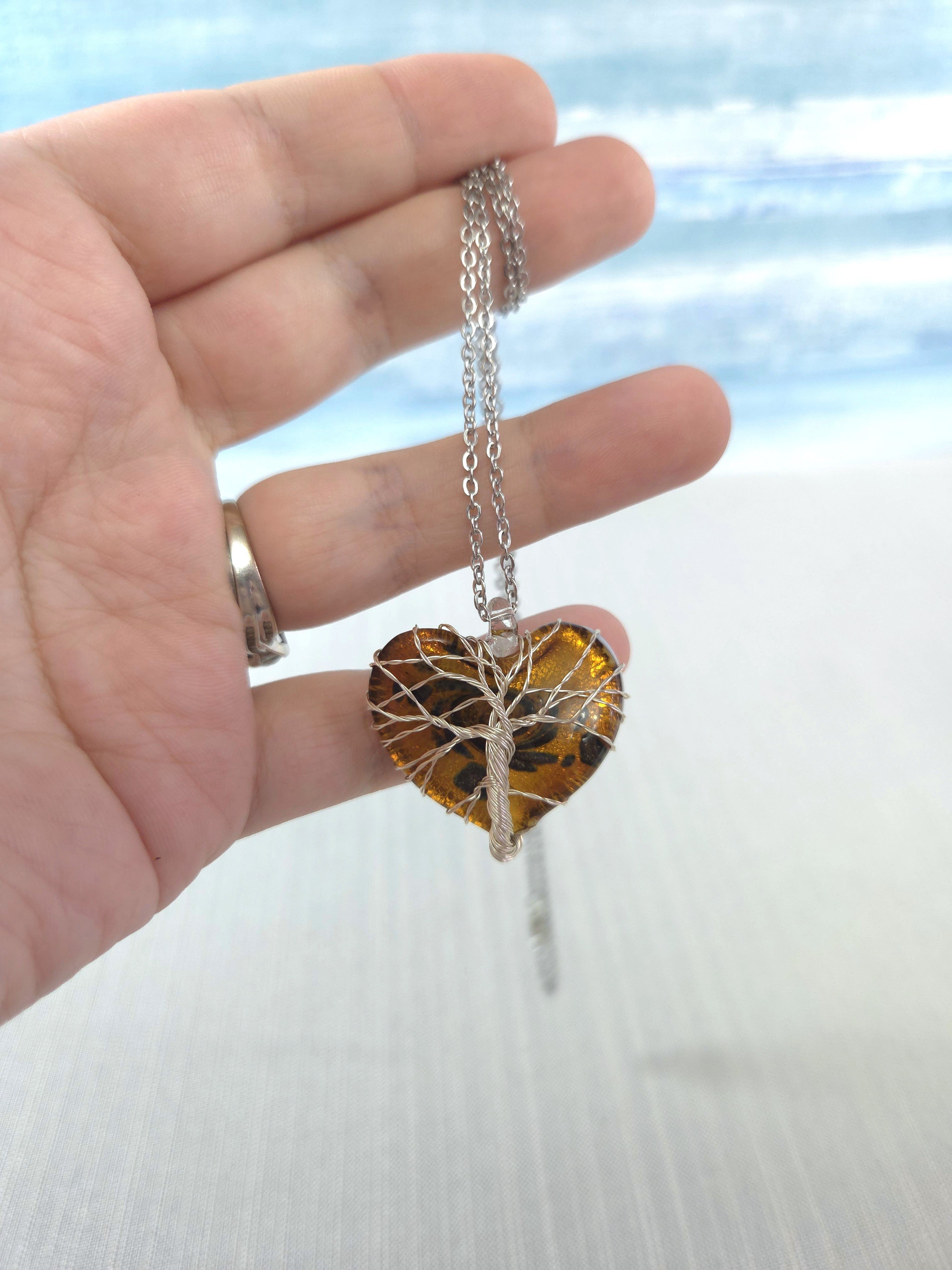 Hand holding a necklace with a heart-shaped amber pendant against a blurred natural background