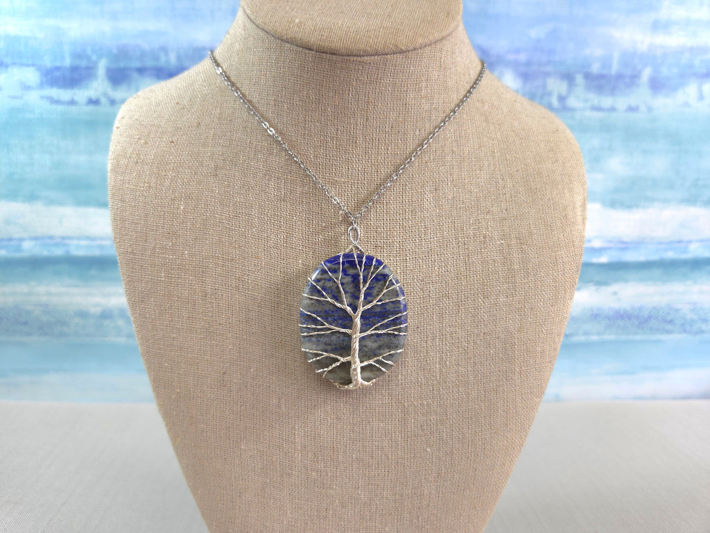 Necklace with a tree-shaped pendant on a mannequin bust against a blurred beach background