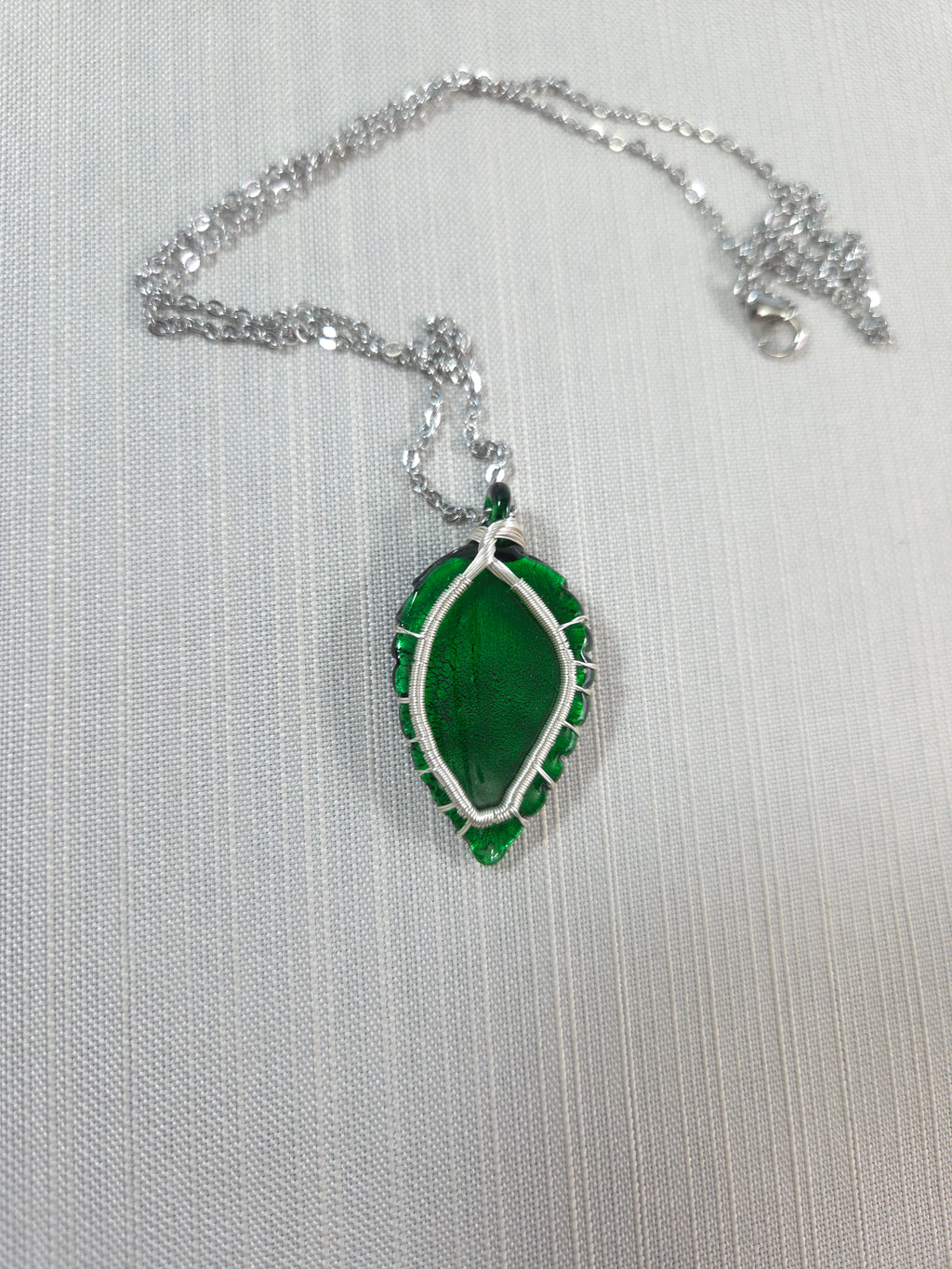 Green leaf-shaped pendant on a silver chain against a white background