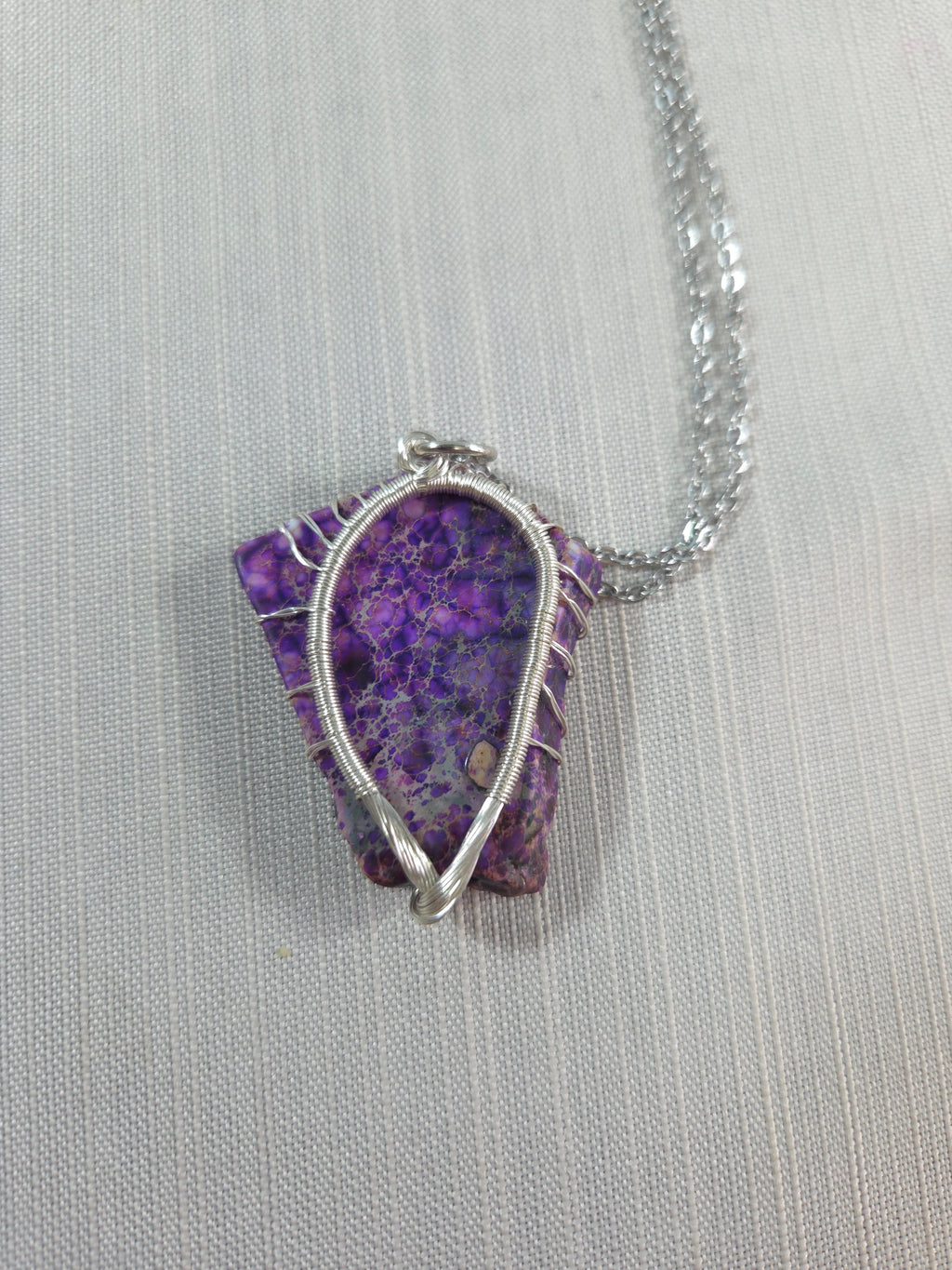 Purple stone pendant with silver wire wrapping on a light gray background