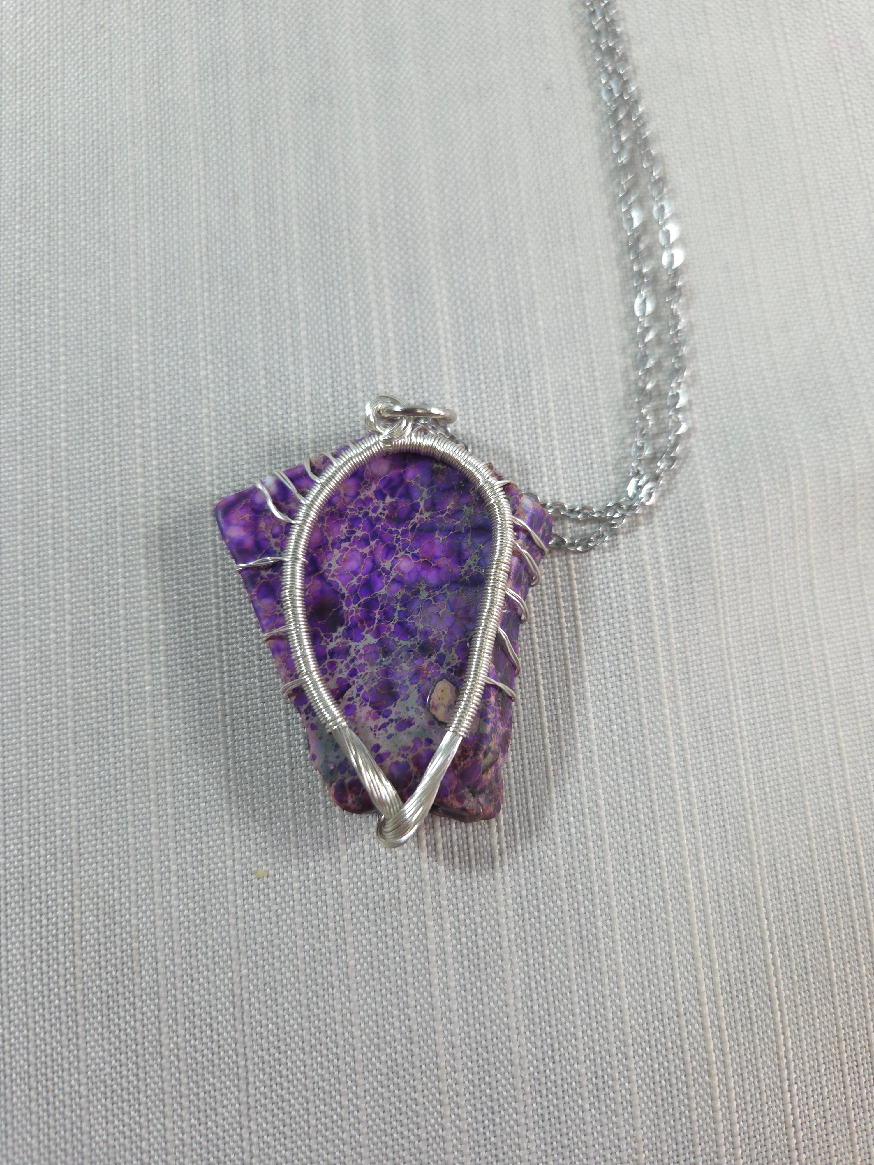 Purple stone pendant with silver wire wrapping on a light gray background