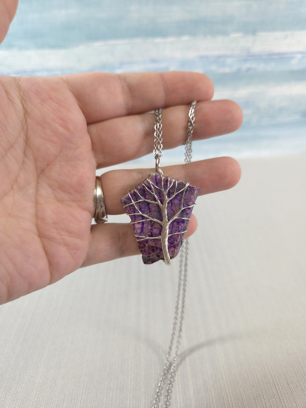 Hand holding a necklace with a purple pendant against a blurred background