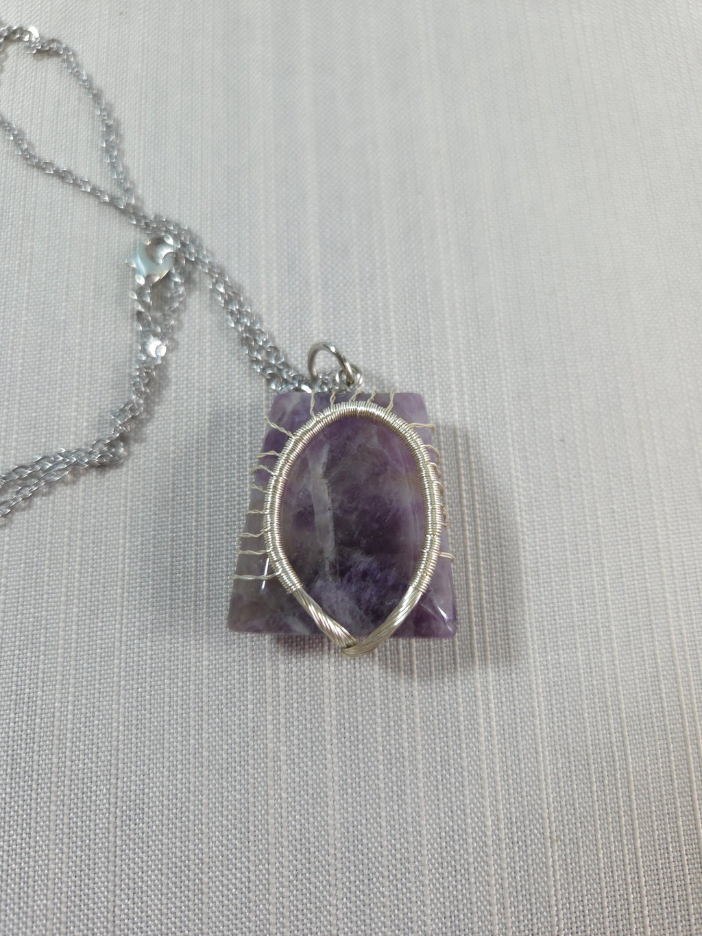 Amethyst pendant with silver chain on a light gray background