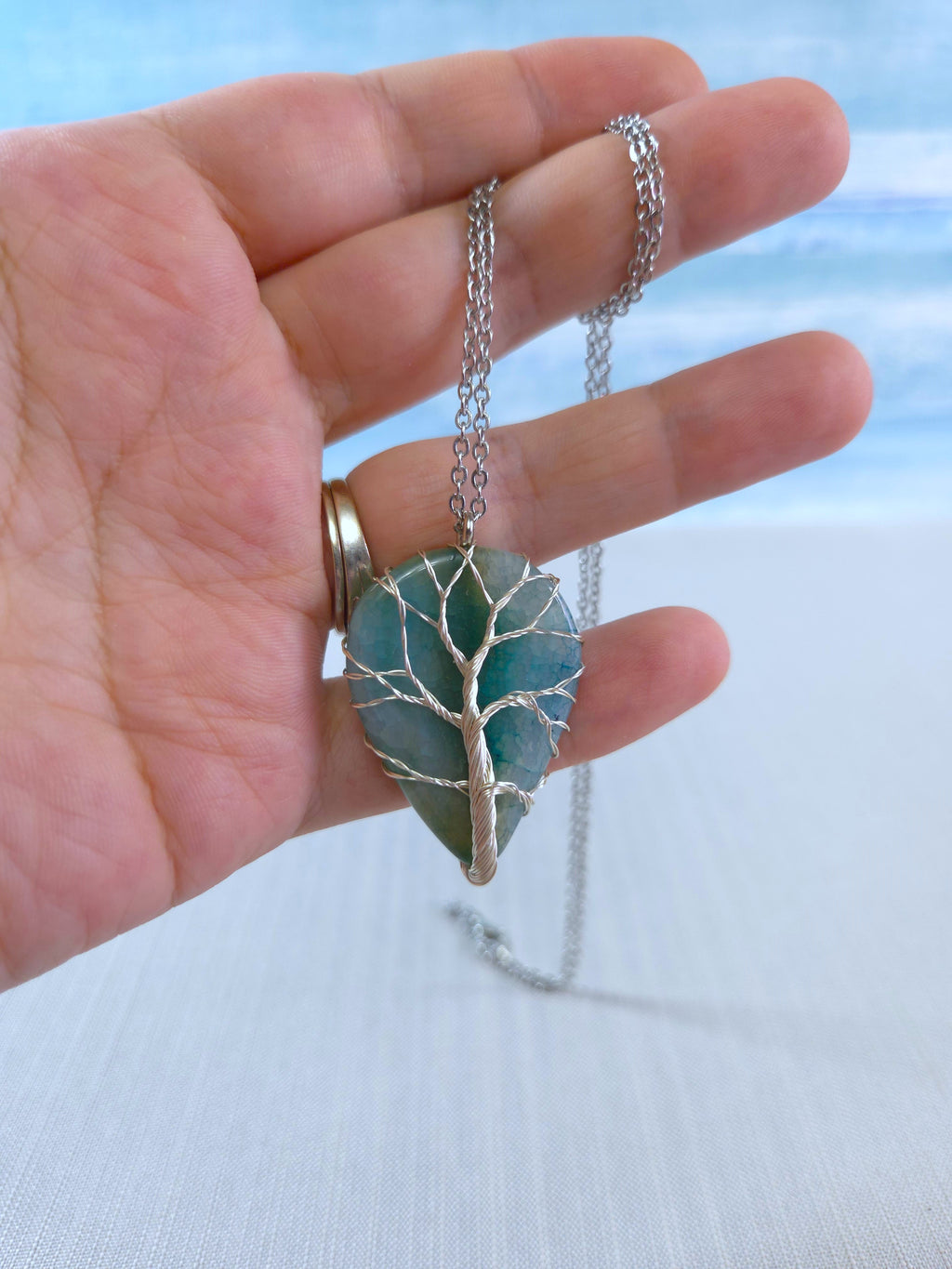 Hand holding a necklace with a leaf-shaped pendant against a light background