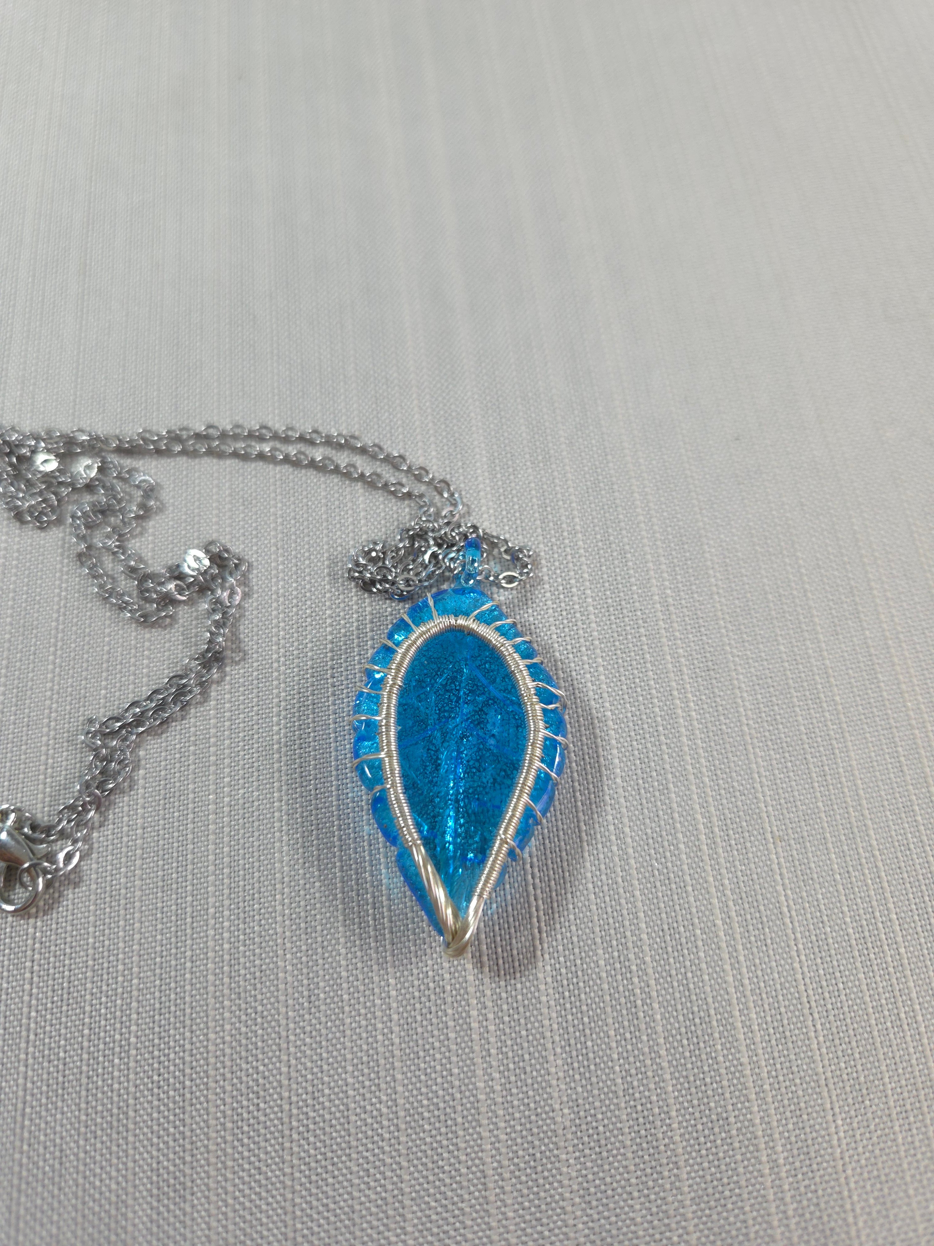 Blue teardrop-shaped pendant on a chain against a gray background