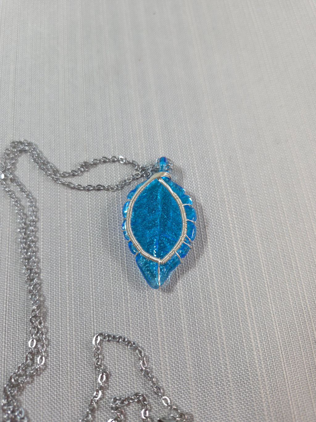 Blue gemstone pendant on a silver chain against a light gray background