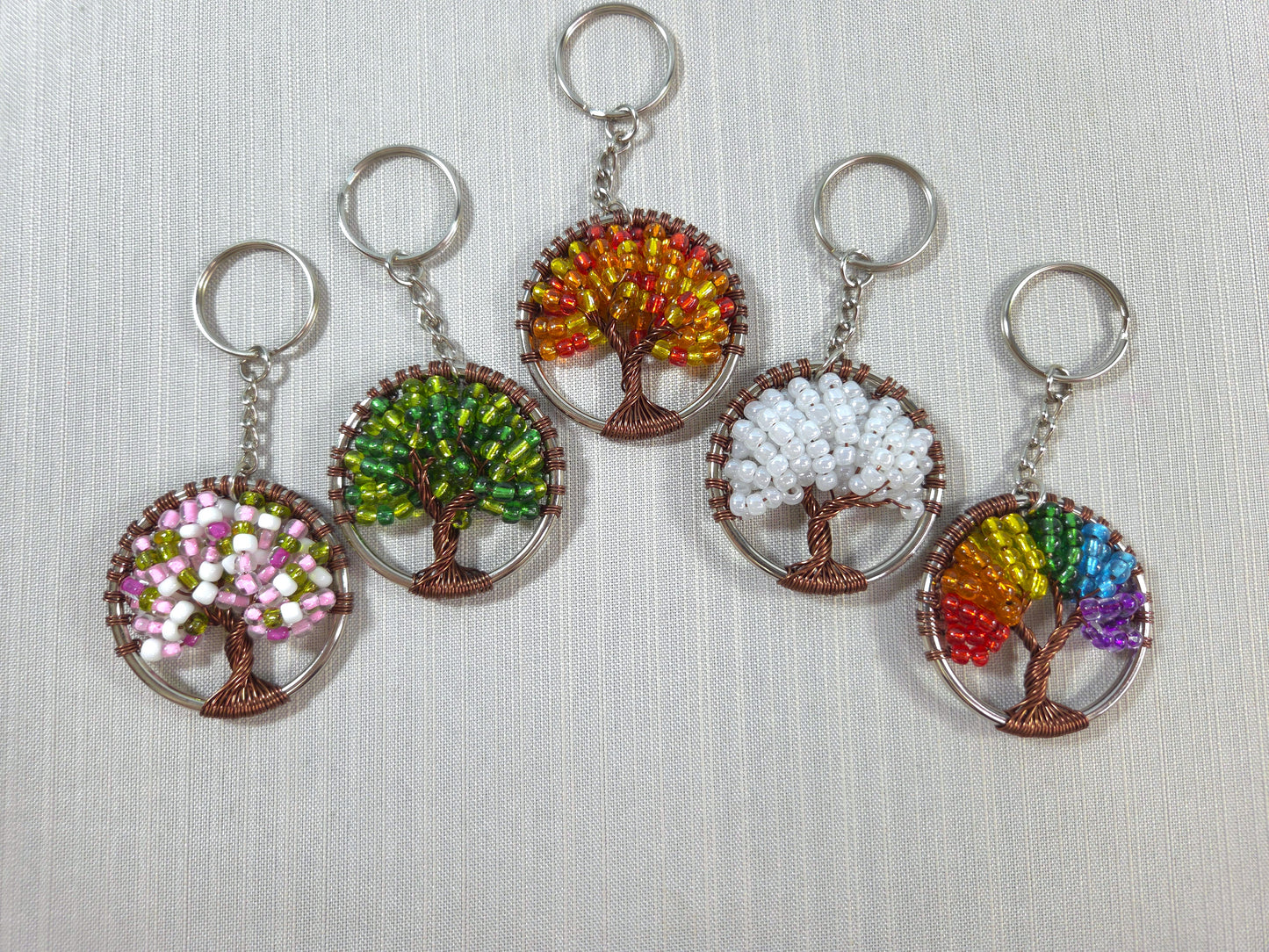 Five tree-shaped keychains with colorful bead designs on a light gray background