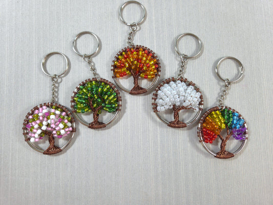 Five tree-shaped keychains with colorful bead designs on a light gray background