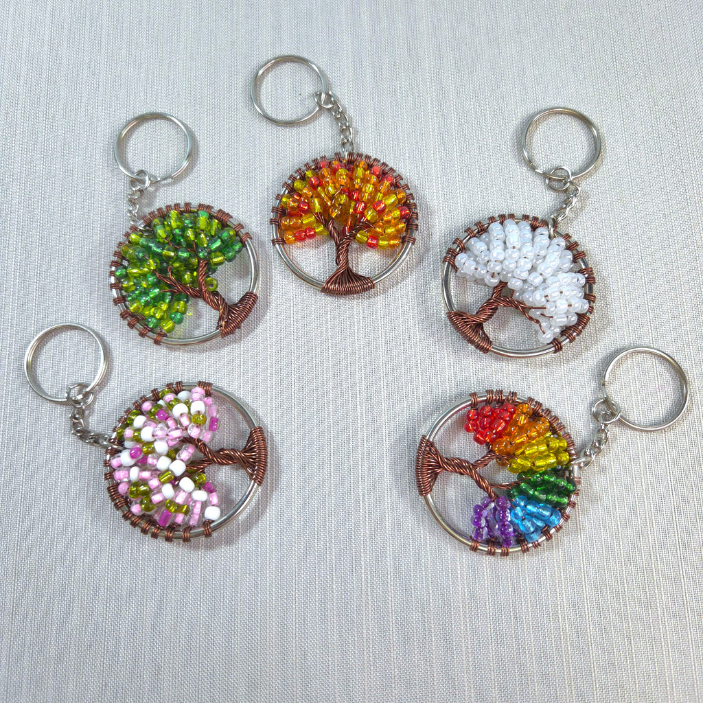 Set of six tree-shaped keychains with colorful bead patterns on a light fabric background.