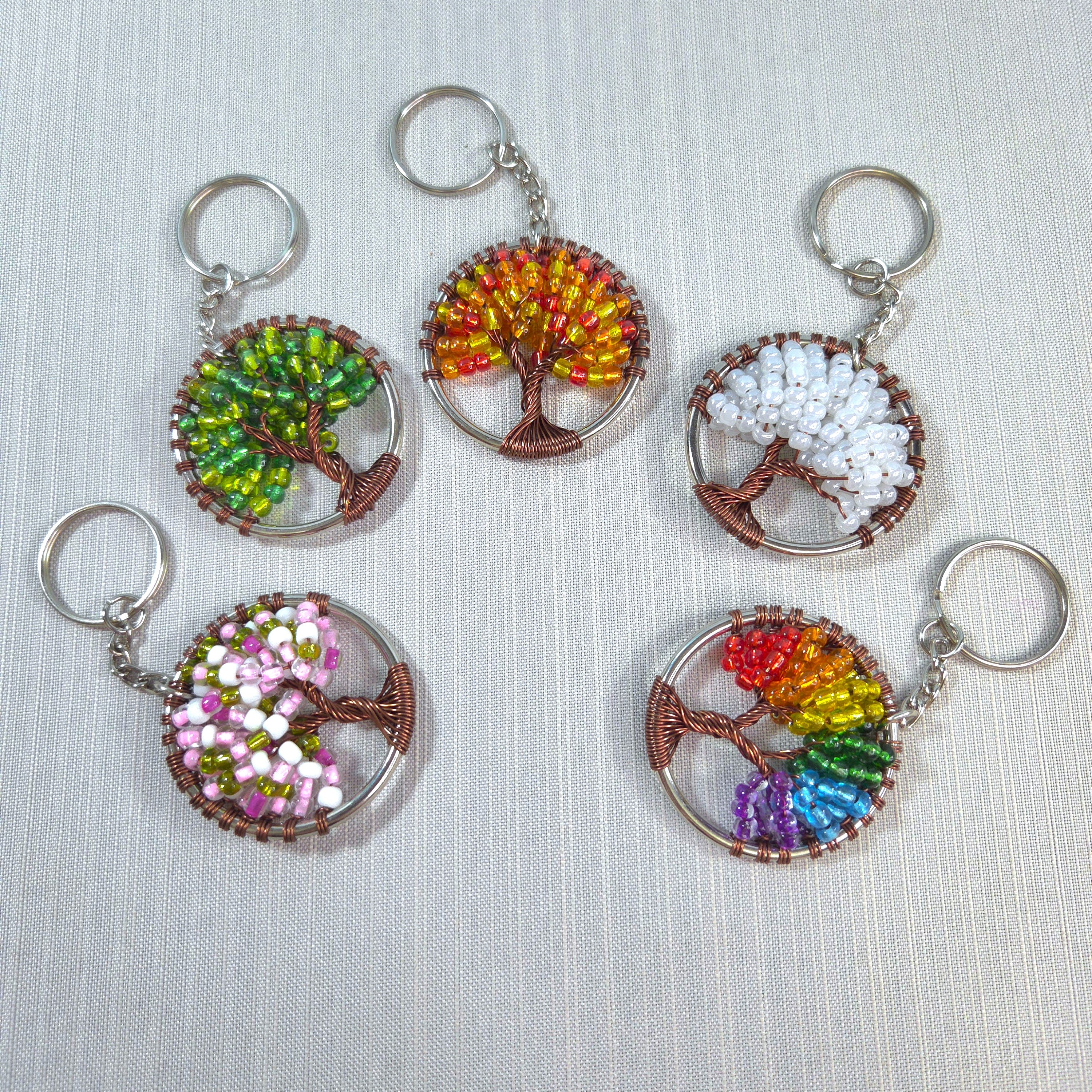 Set of six tree-shaped keychains with colorful bead patterns on a light fabric background.