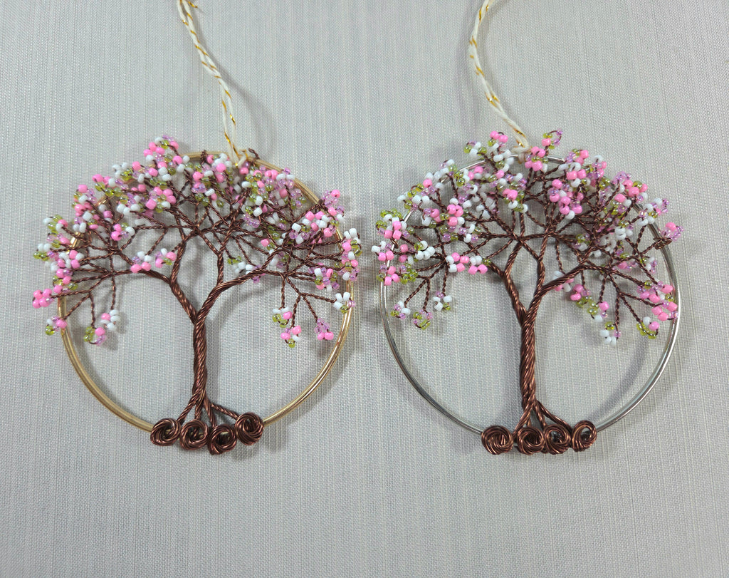 Pair of tree-shaped earrings with pink and white bead decorations on a light gray background.