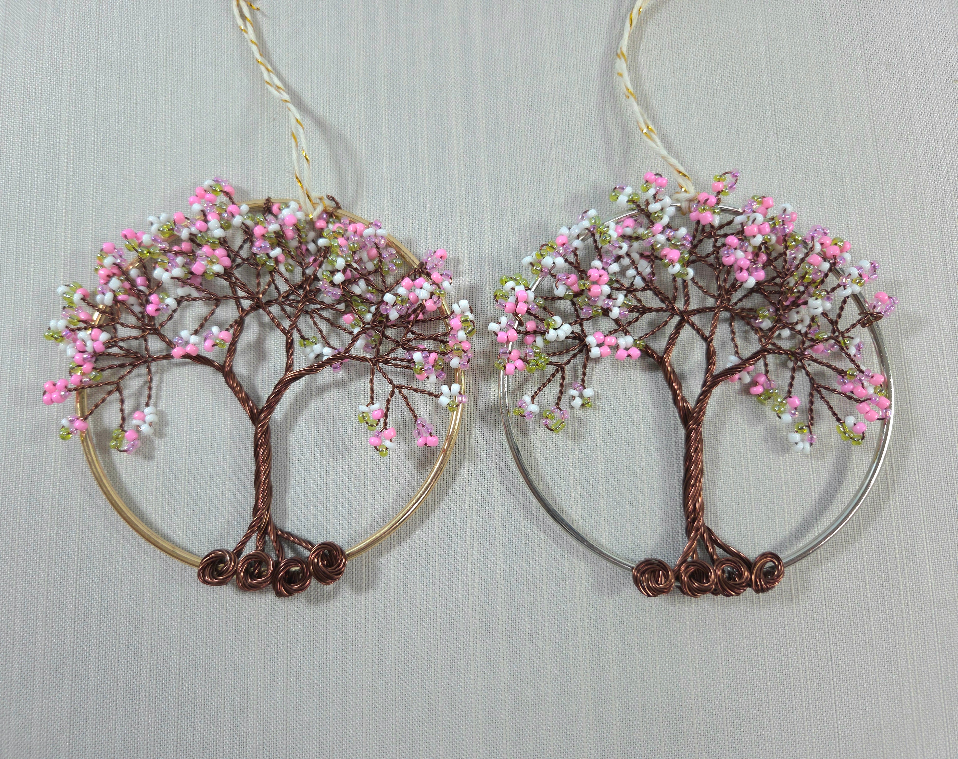 Pair of tree-shaped earrings with pink and white bead decorations on a light gray background.