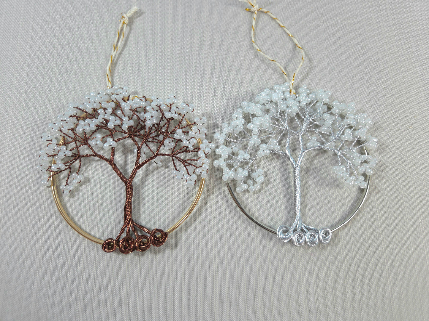 Two tree-shaped earrings, one gold and one silver, on a light gray background.