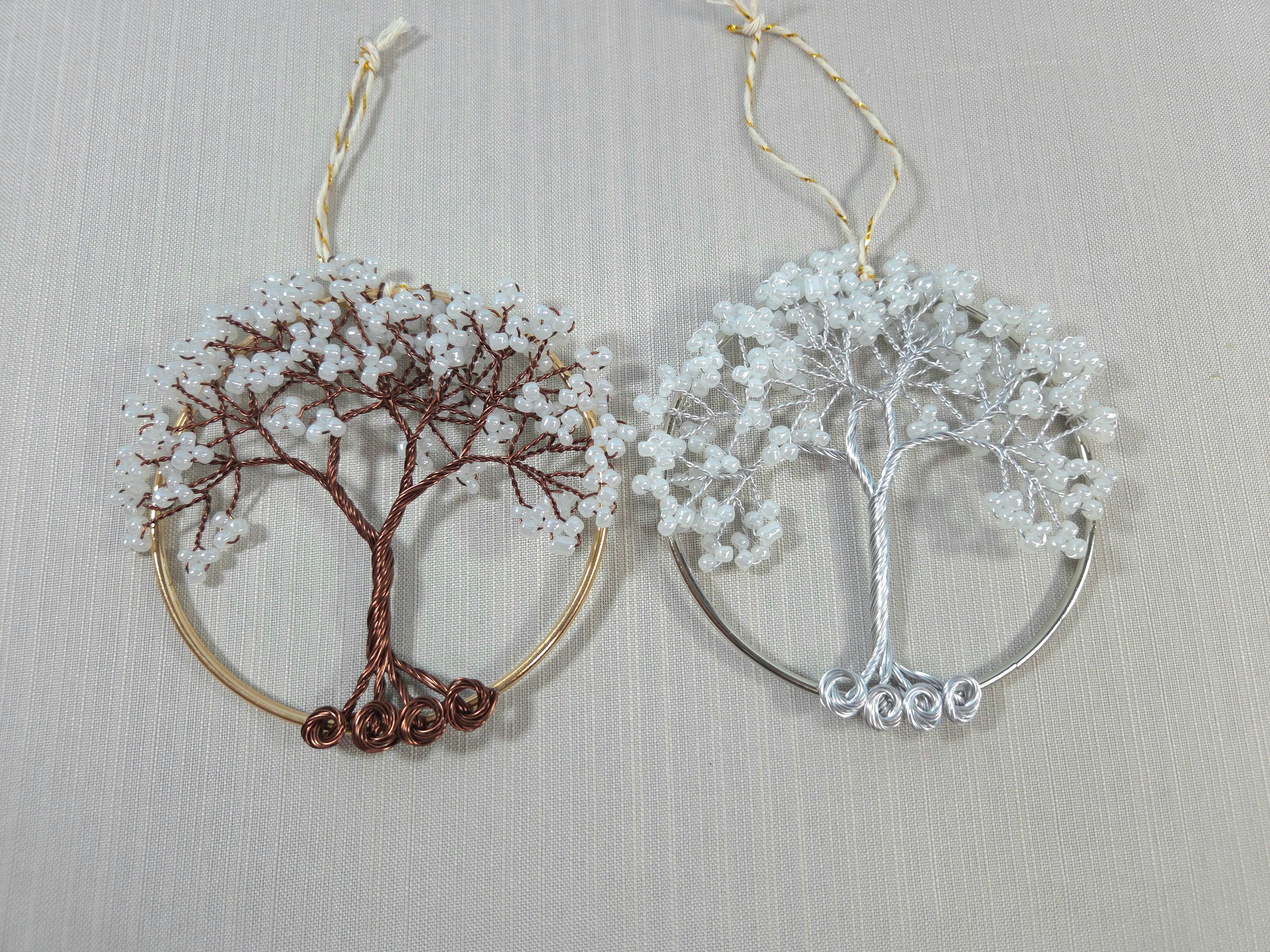 Two tree-shaped earrings, one gold and one silver, on a light gray background.