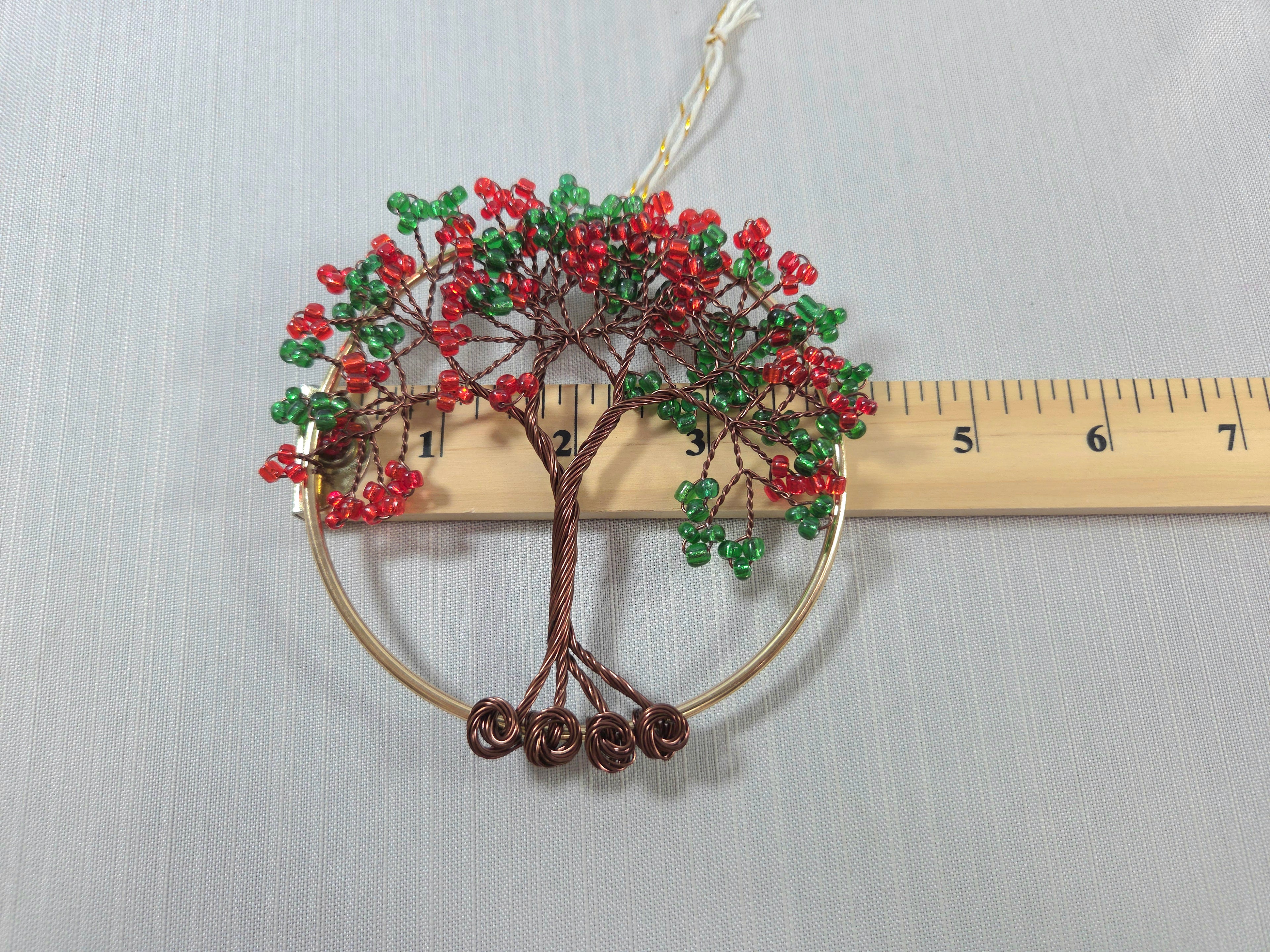 Decorative tree ornament with red and green beads next to a ruler on a light gray background