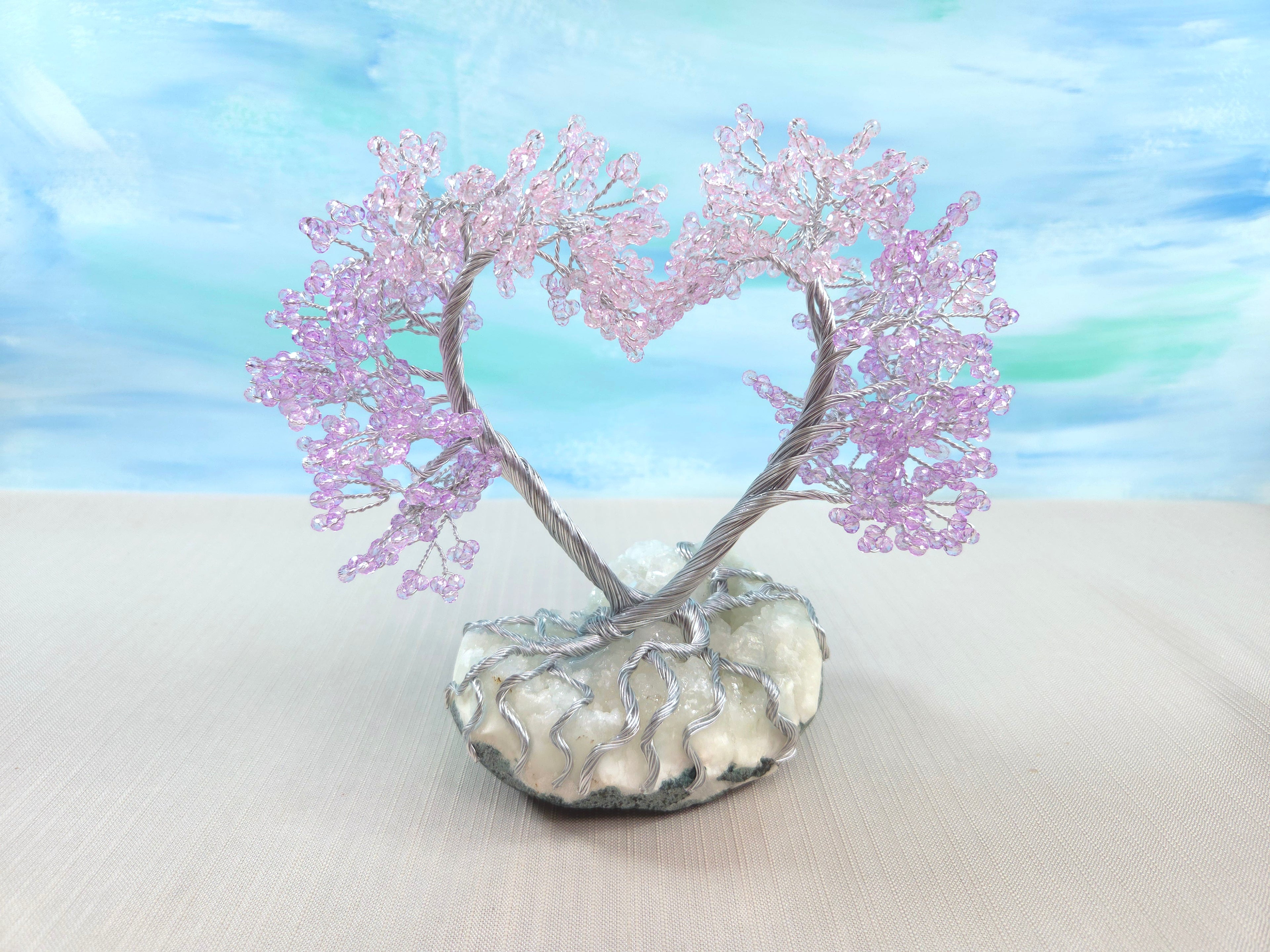 Decorative heart-shaped tree with pink branches on a white base against a blue sky background