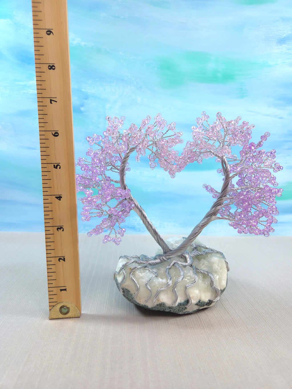 Decorative tree with pink branches in a glass vase on a white surface with a blue gradient background.