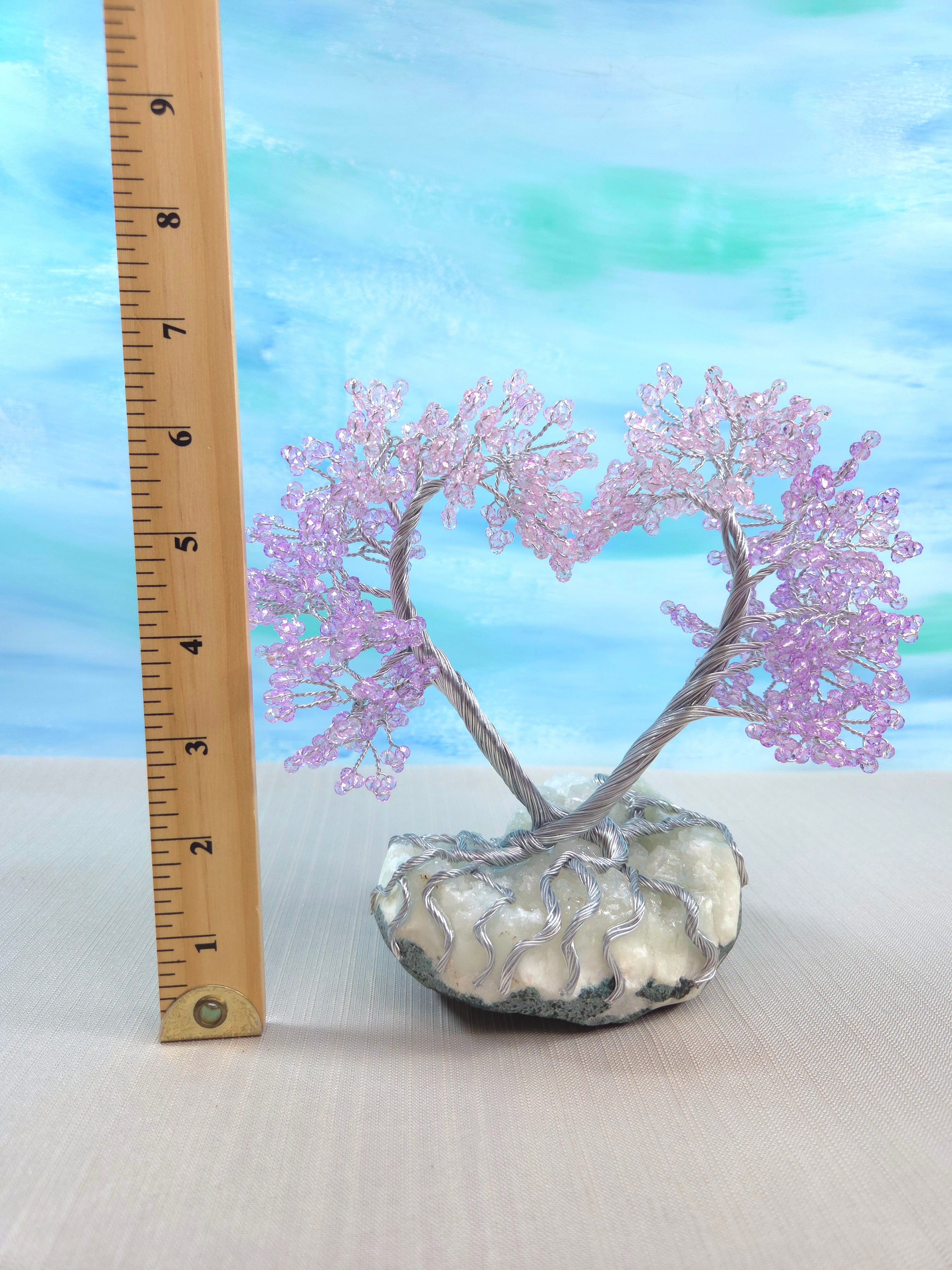 Decorative tree with pink branches in a glass vase on a white surface with a blue gradient background.