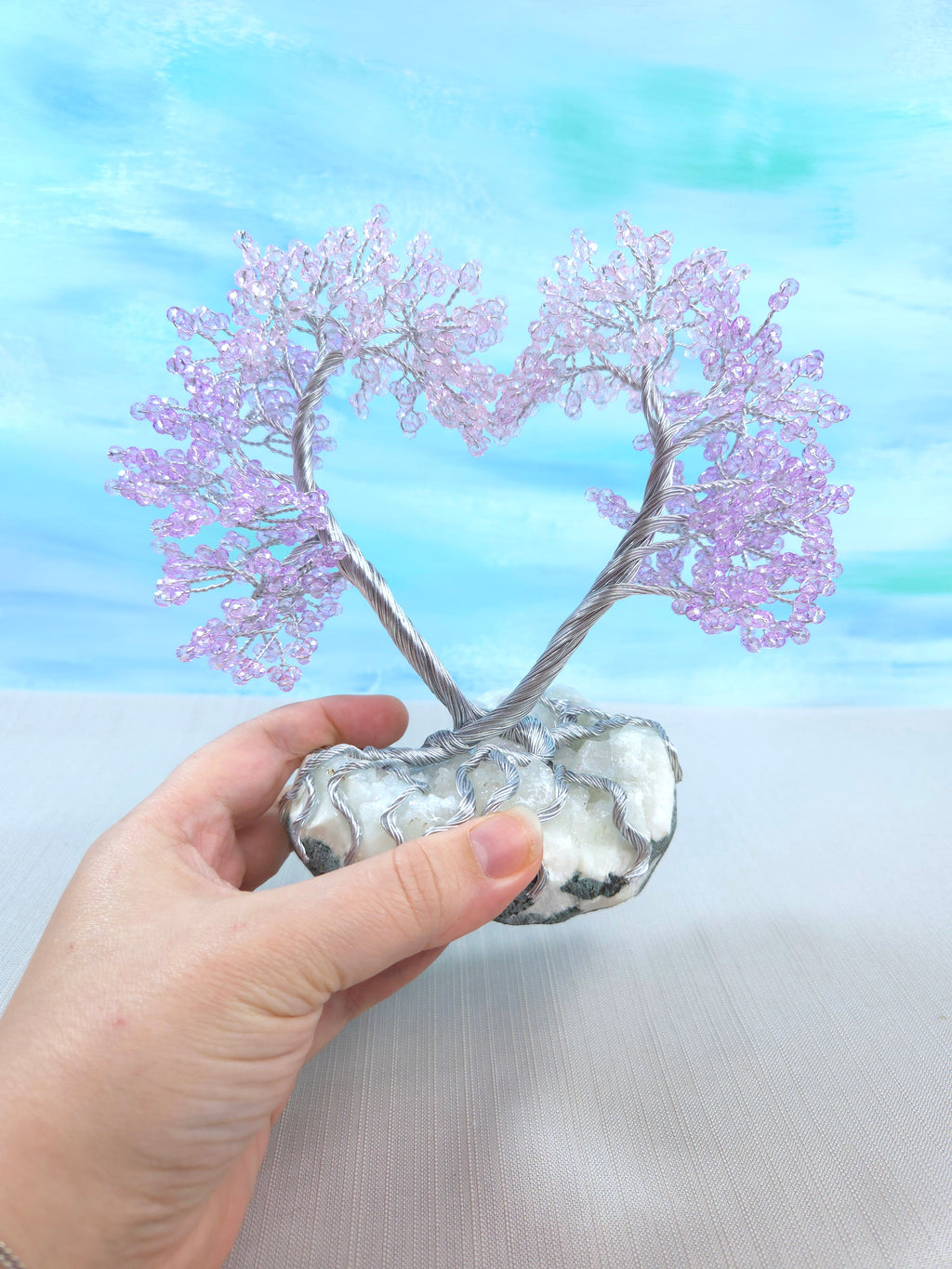 Hand holding a small tree with pink leaves against a blue and white gradient background