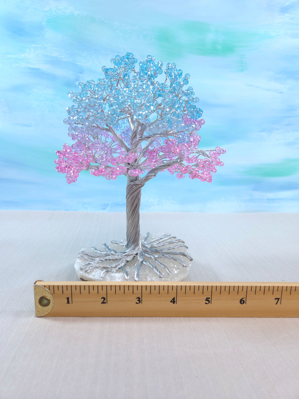Decorative tree with pink and blue branches on a white surface with a ruler for scale.