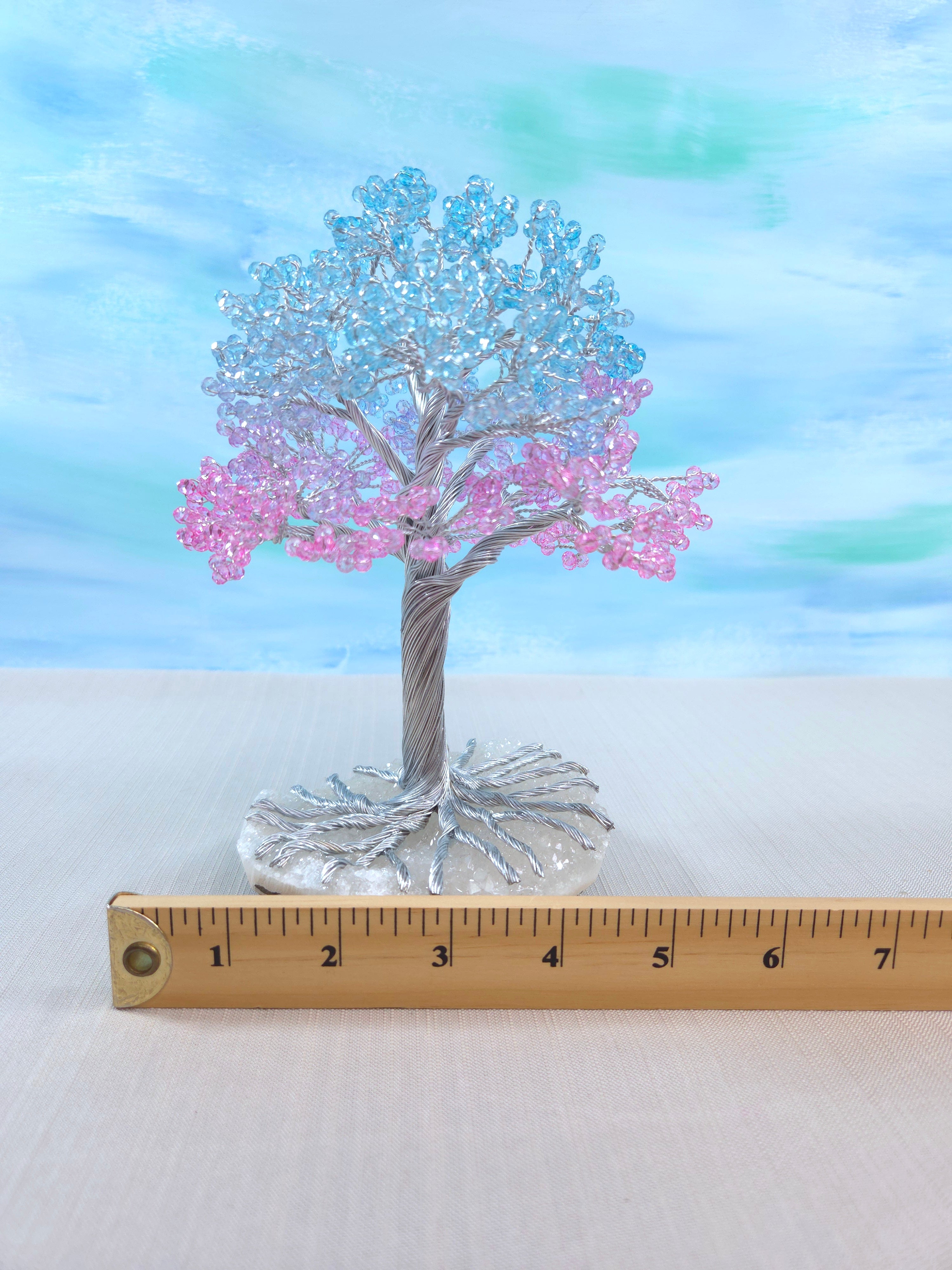 Decorative tree with pink and blue branches on a white surface with a ruler for scale.