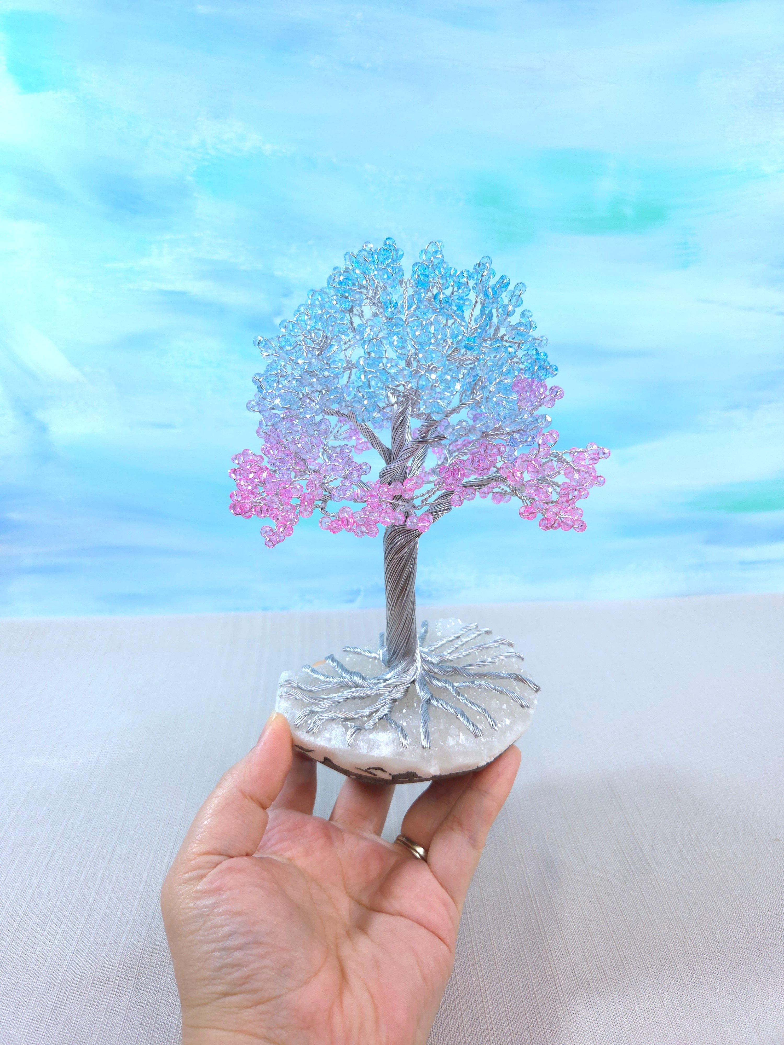 Decorative tree figurine with pink leaves held by a hand against a blurred background