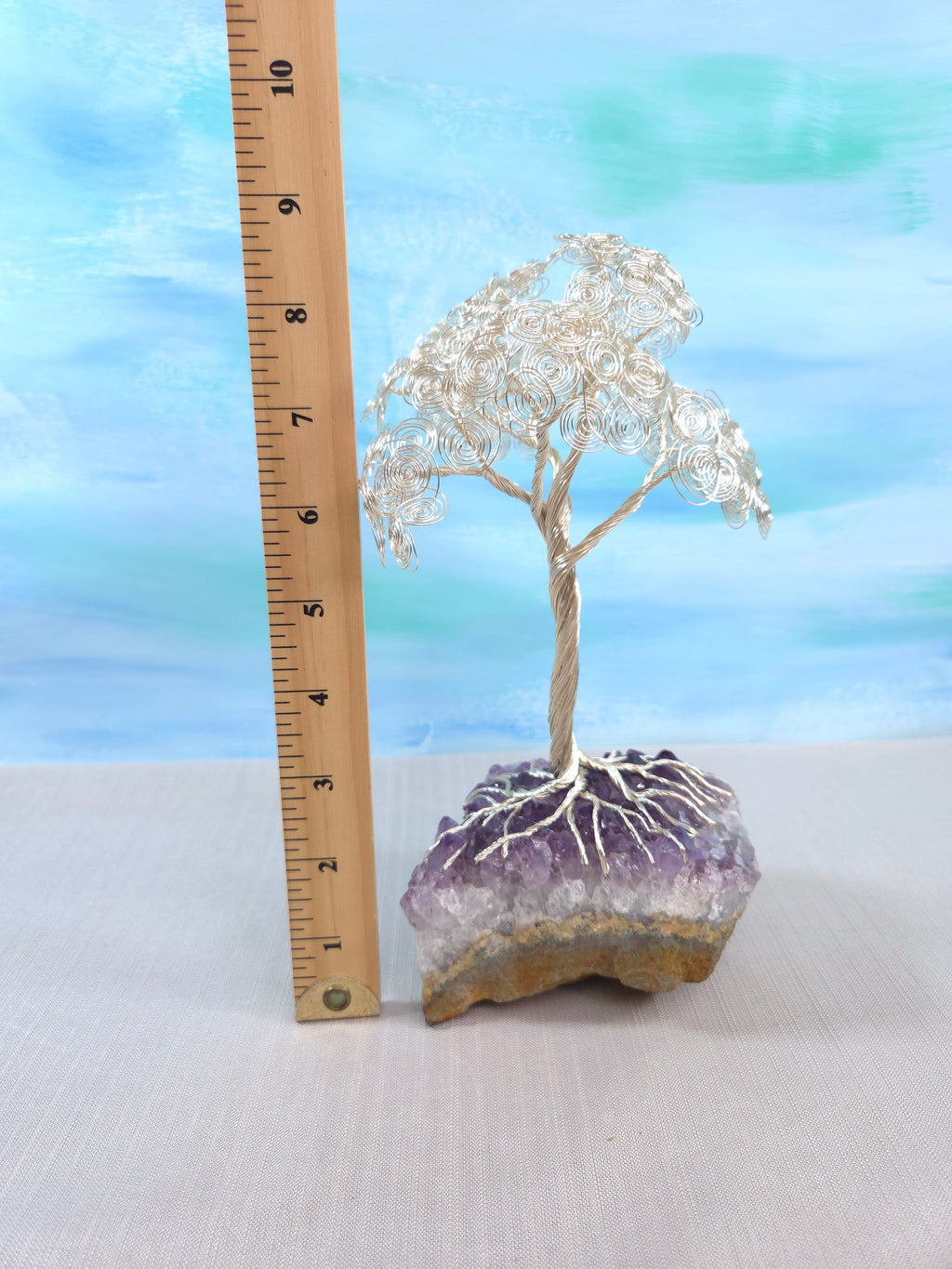 Decorative crystal tree on a purple crystal base with a ruler for scale against a light blue background.