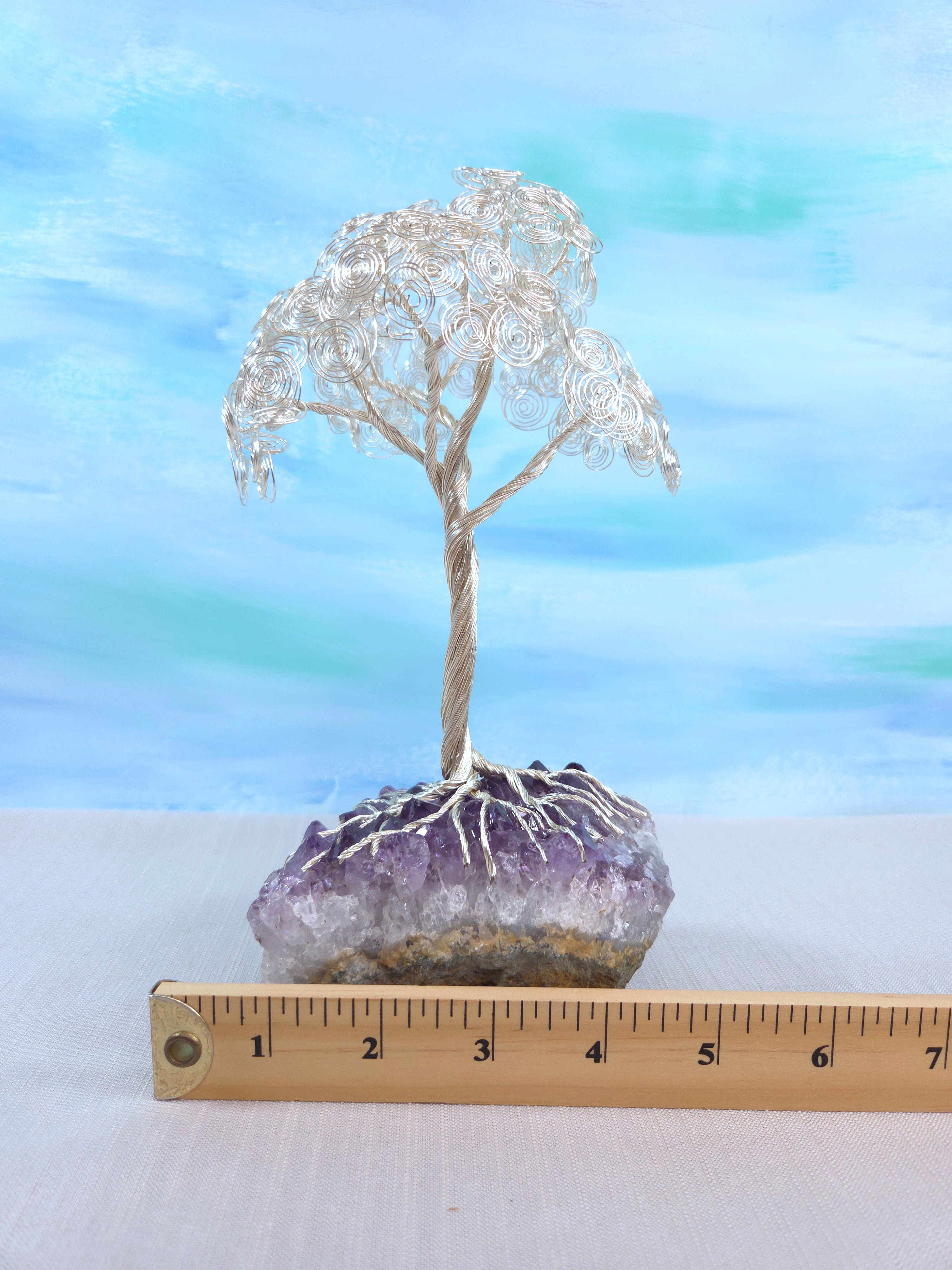 Silver wire tree on a purple crystal with a ruler for scale against a blue gradient background