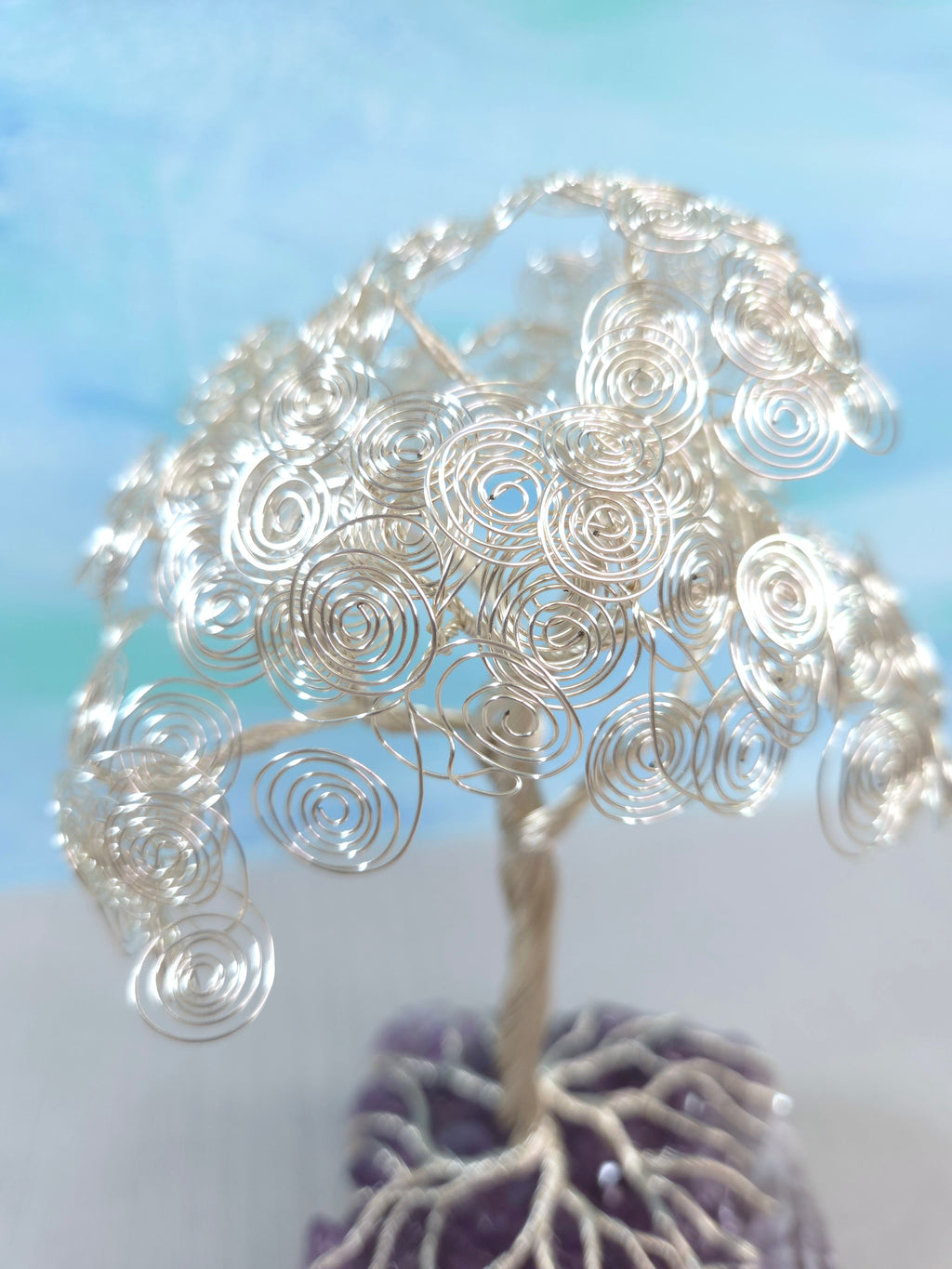 Silver wire tree sculpture with purple base against a light blue background